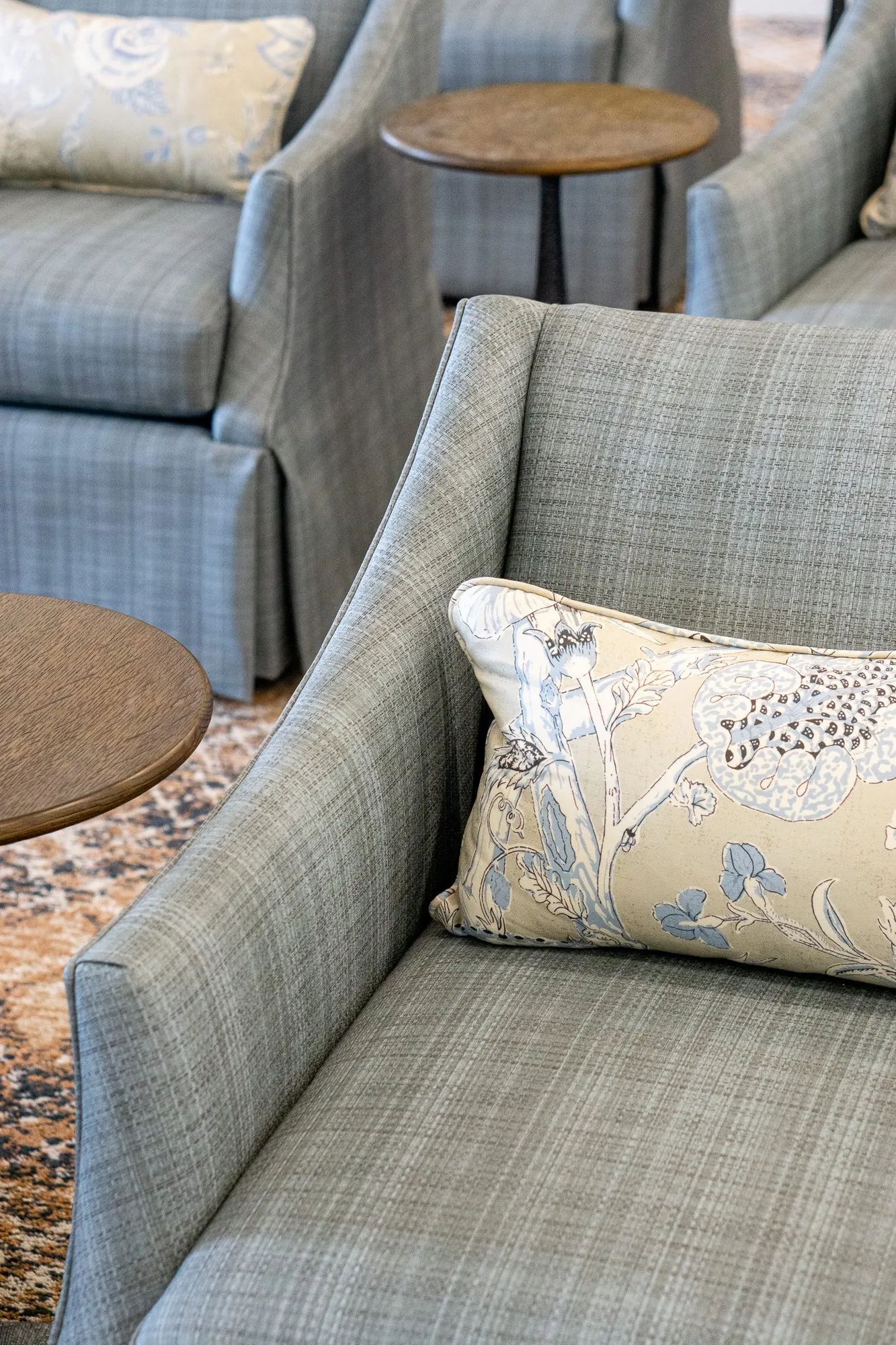 Senior living interior detail: grey plaid armchair with a floral lumbar pillow, more armchairs beyond
