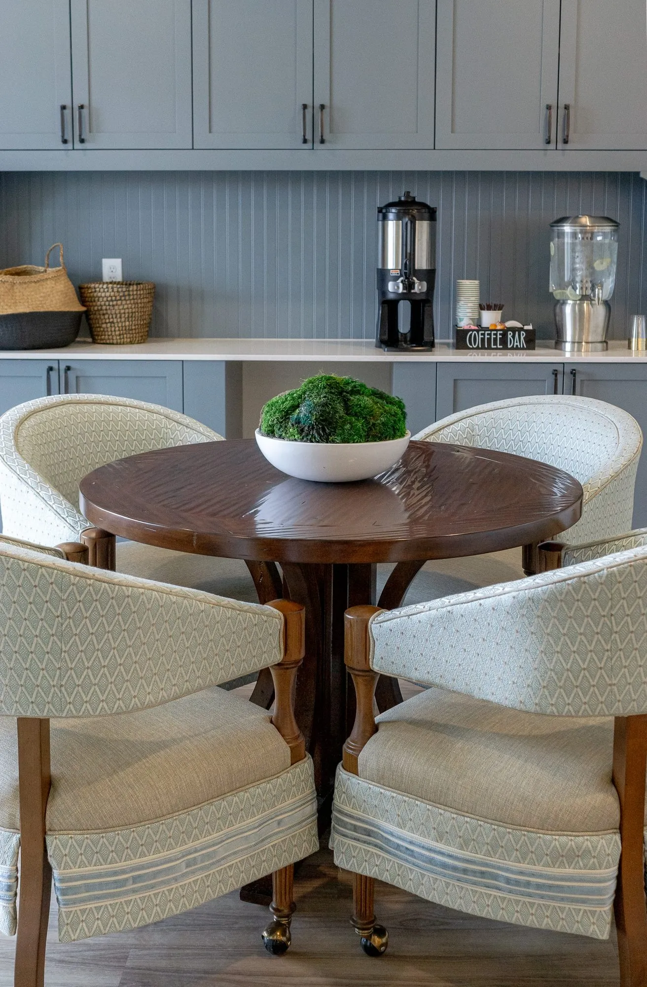 Senior living coffee station with four pale blue barrel chairs around a walnut table with a moss bowl