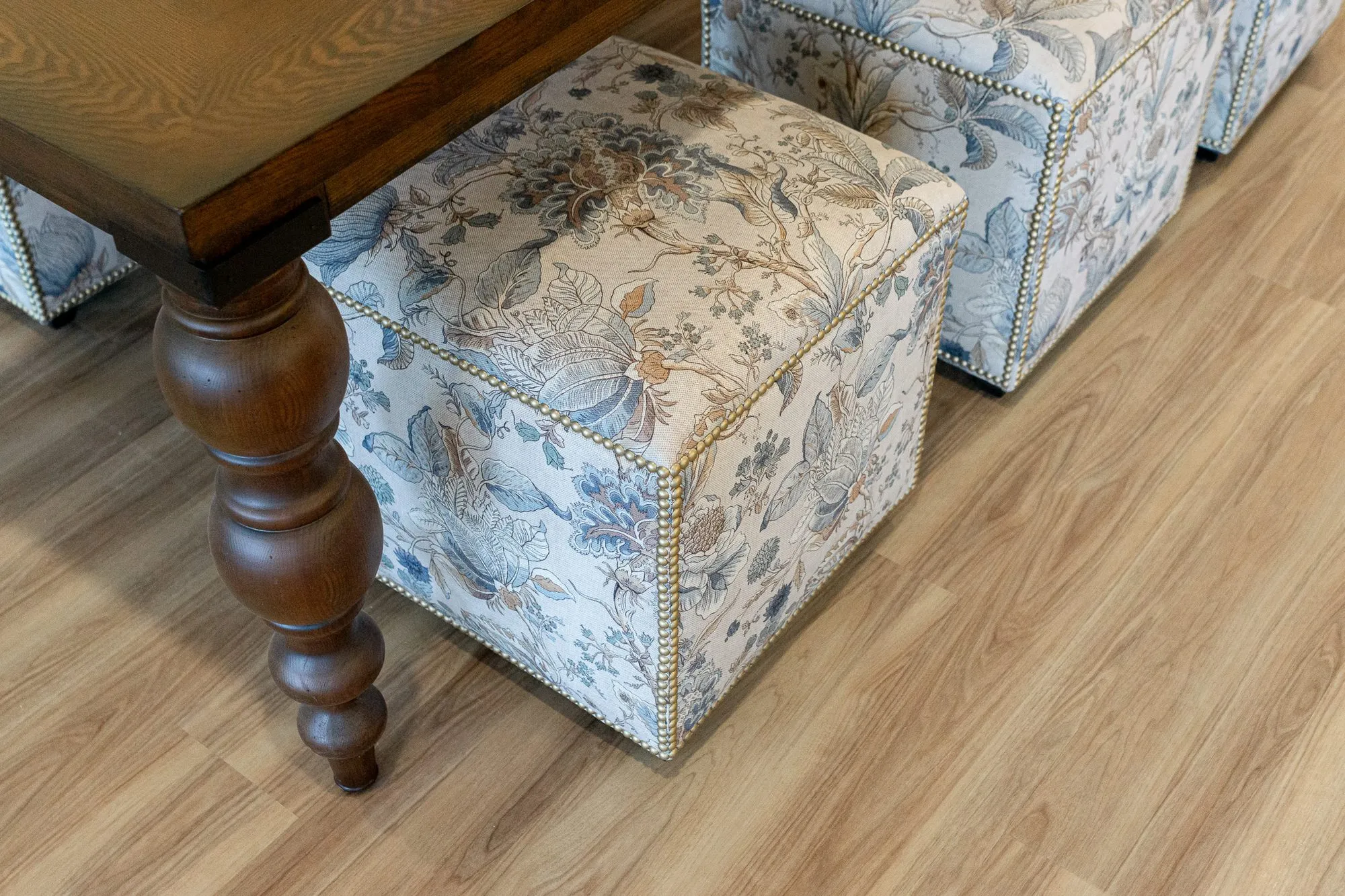 Senior living interior detail: high angle view of a floral cube ottoman with nailhead trim by a turned walnut table leg