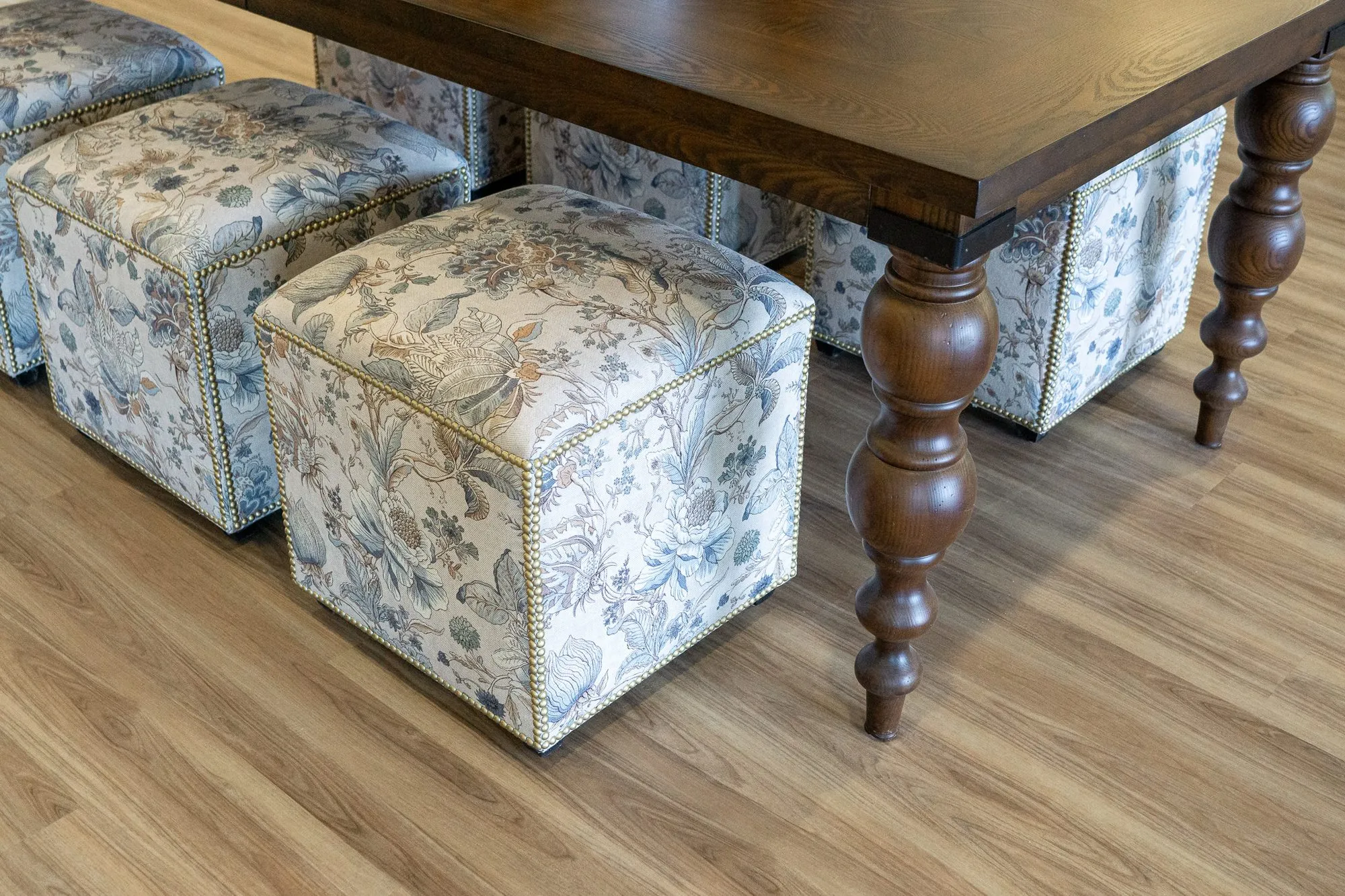 Senior living interior detail: low view of floral cube ottomans tucked beneath a walnut table with turned legs