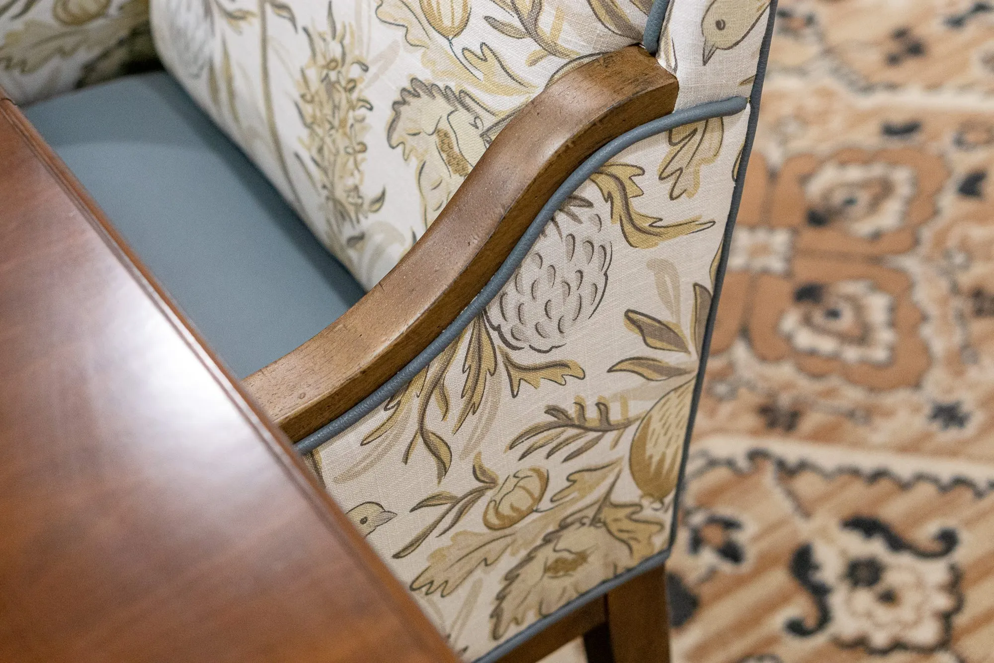 Senior living interior detail: bird print dining chair's curved wood arm and blue seat beside the table