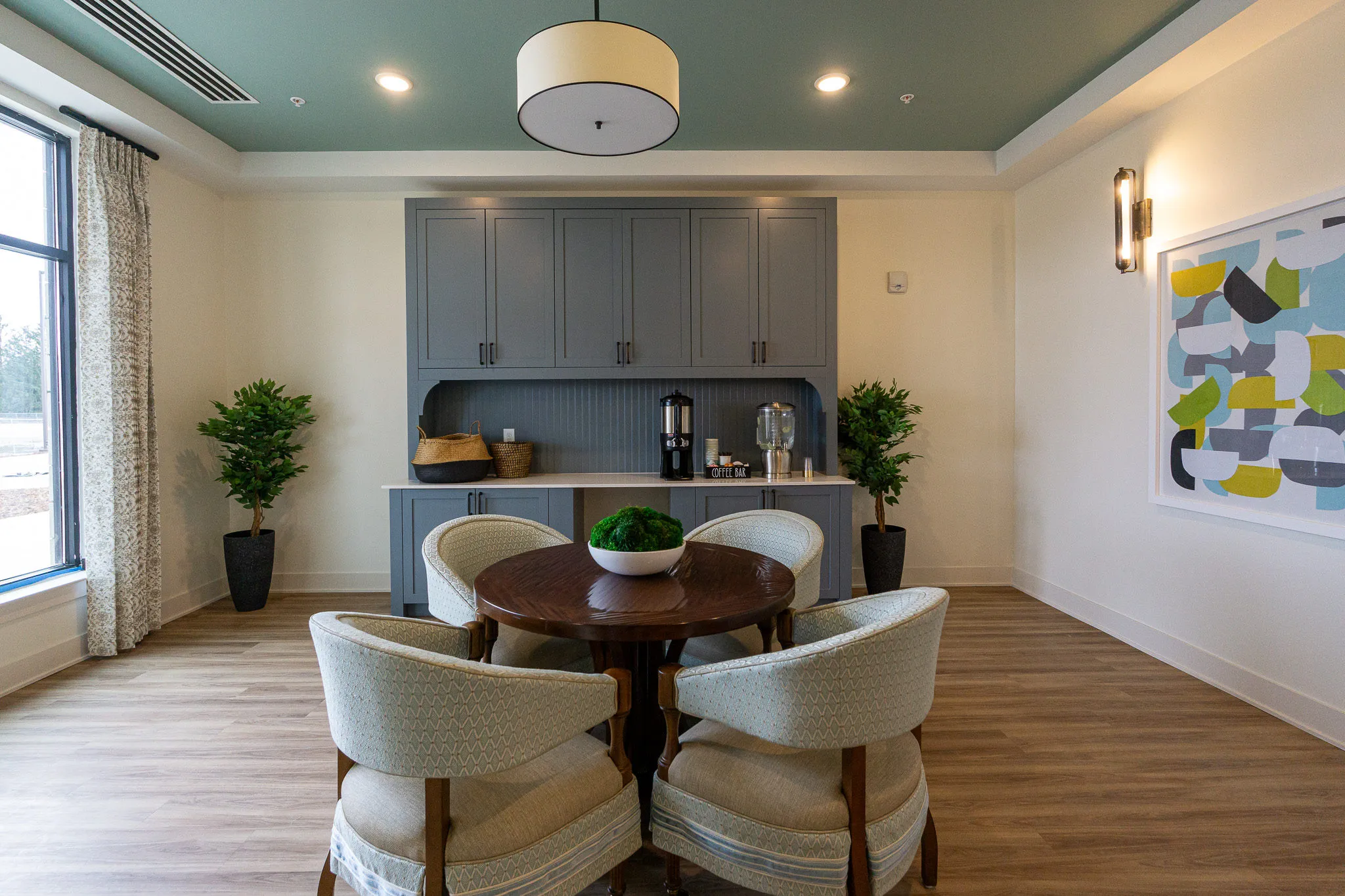 Senior living coffee bar with grey-blue cabinetry and a coffee station behind a round table with skirted barrel chairs