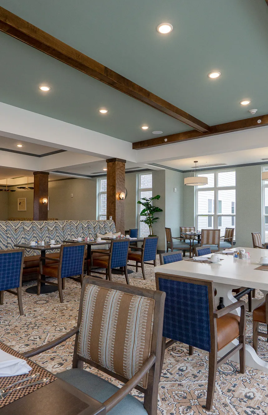 Senior living dining room under a sage vaulted ceiling with dark timber beams, interior design by Banko Design at American House Meridian, Haslett, Michigan