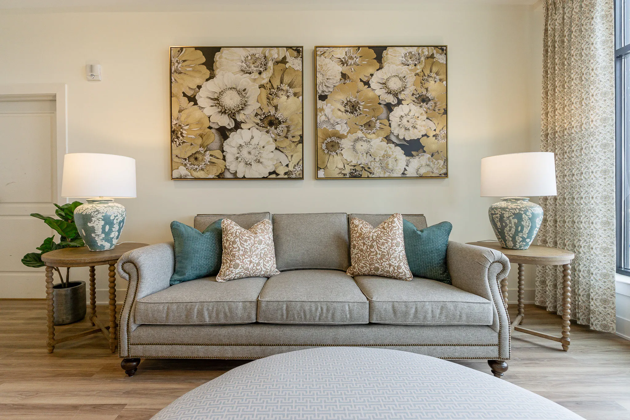Senior living lounge with a rolled-arm sofa and teal pillows below two oversized floral canvases