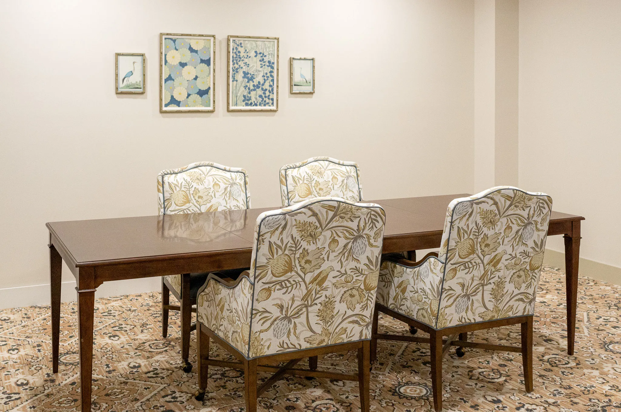 Senior living private dining room with floral upholstered chairs along a walnut table below framed botanicals