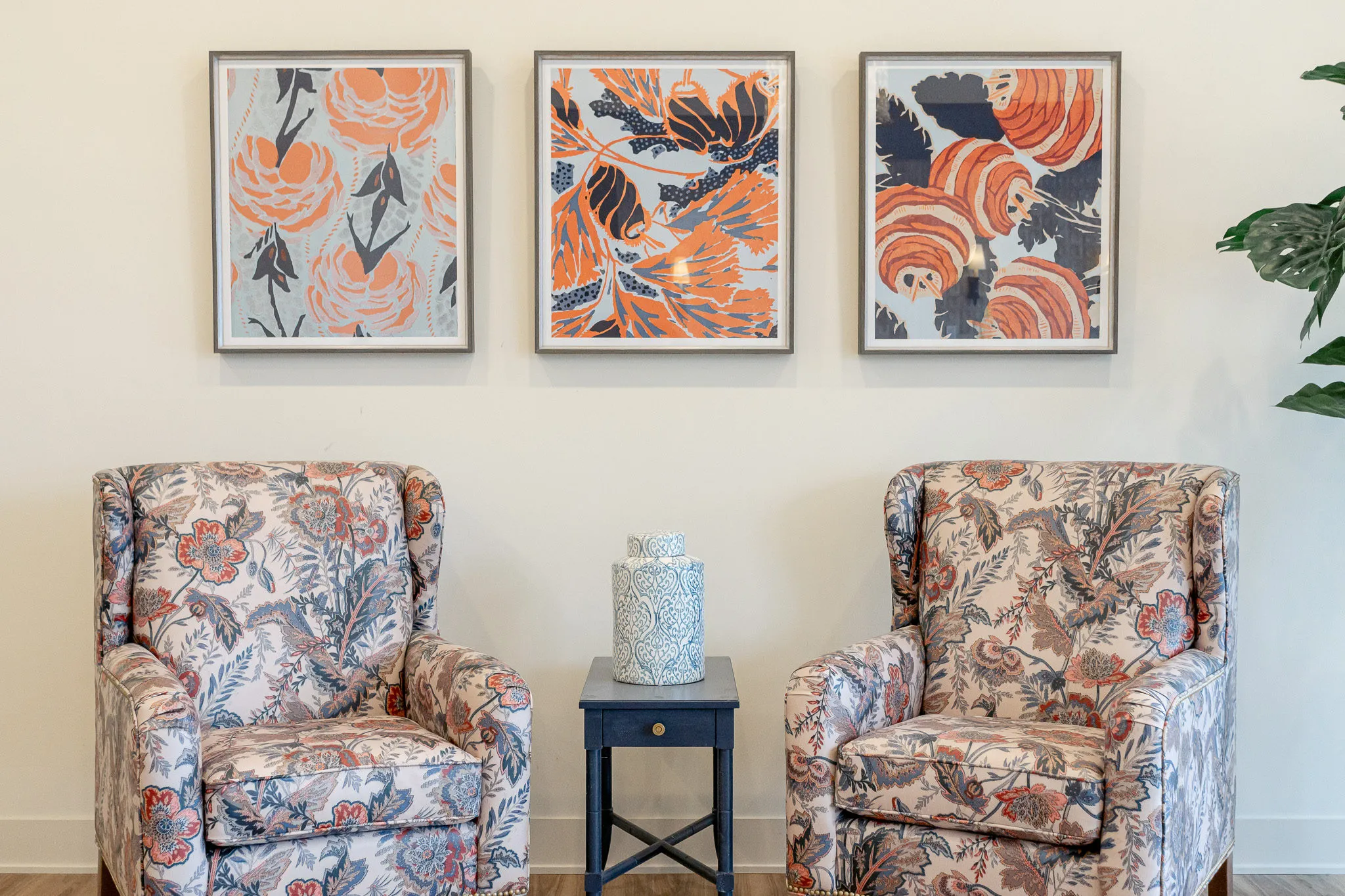 Senior living sitting area with floral wing chairs either side of a navy drink table under three floral prints