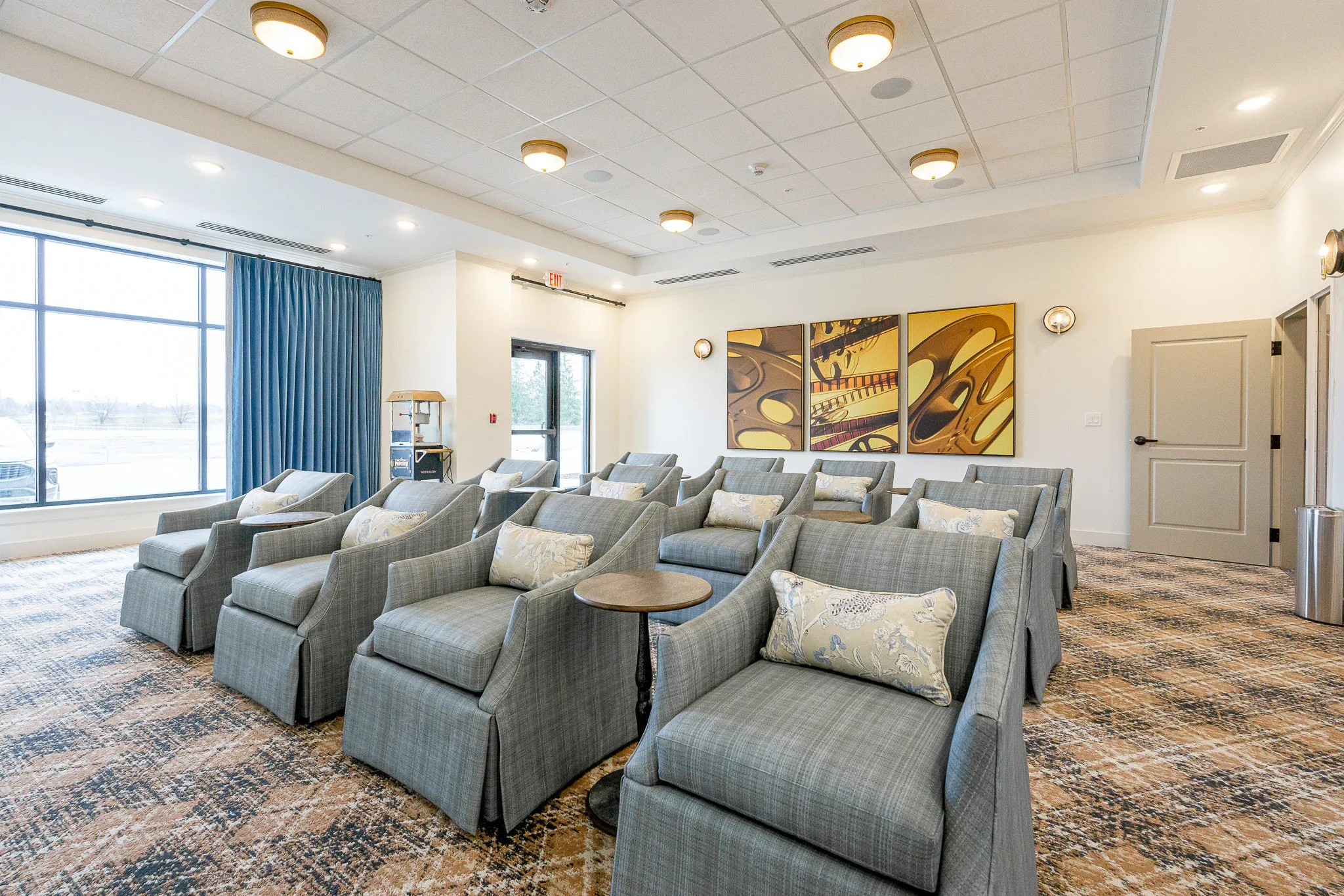 Senior living theater with rows of grey skirted armchairs facing the jazz triptych beside the window wall