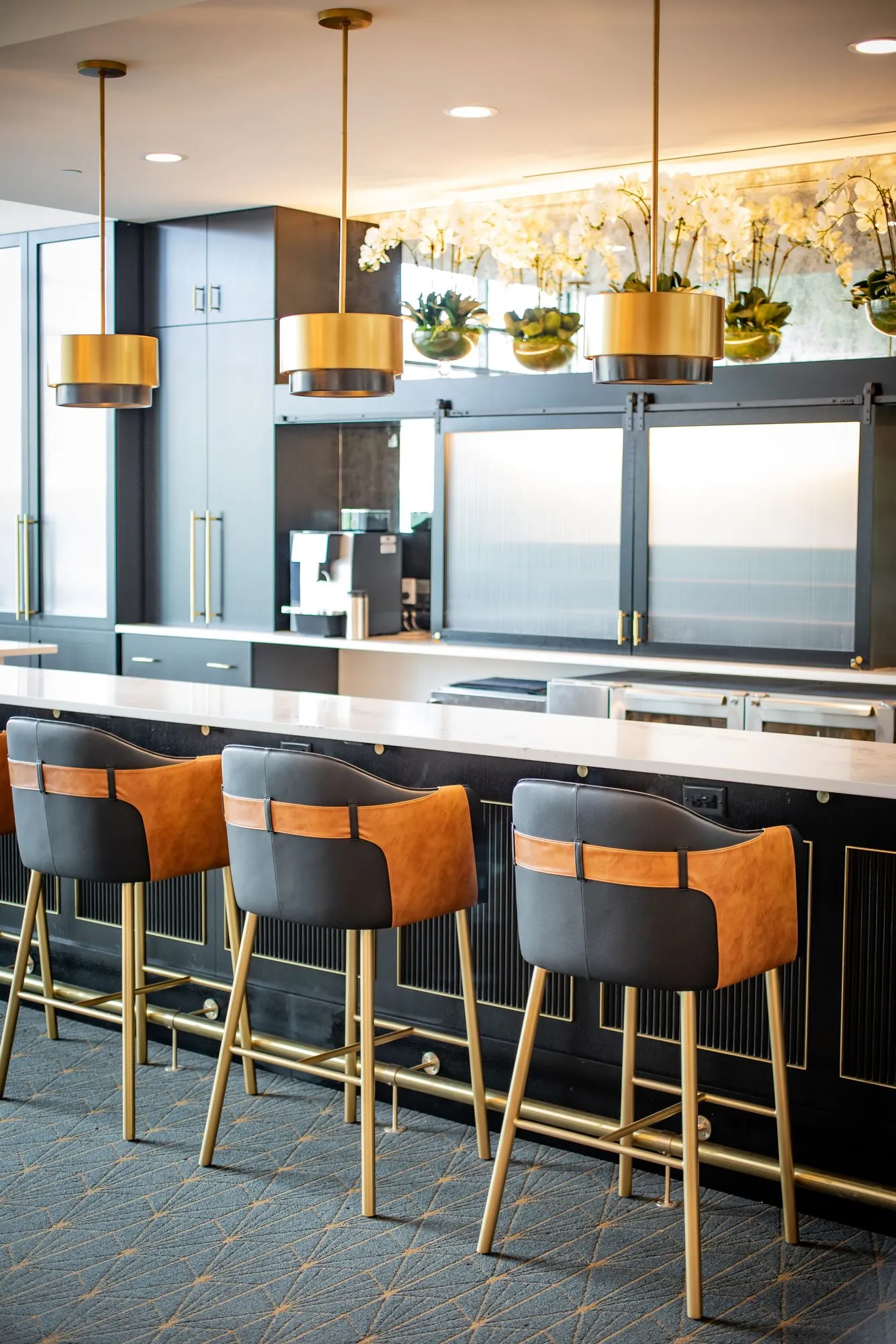 Senior living bar with two-tone leather stools under brass drum pendants, interior design by Banko Design at American House Oak Park, Oak Park, Illinois