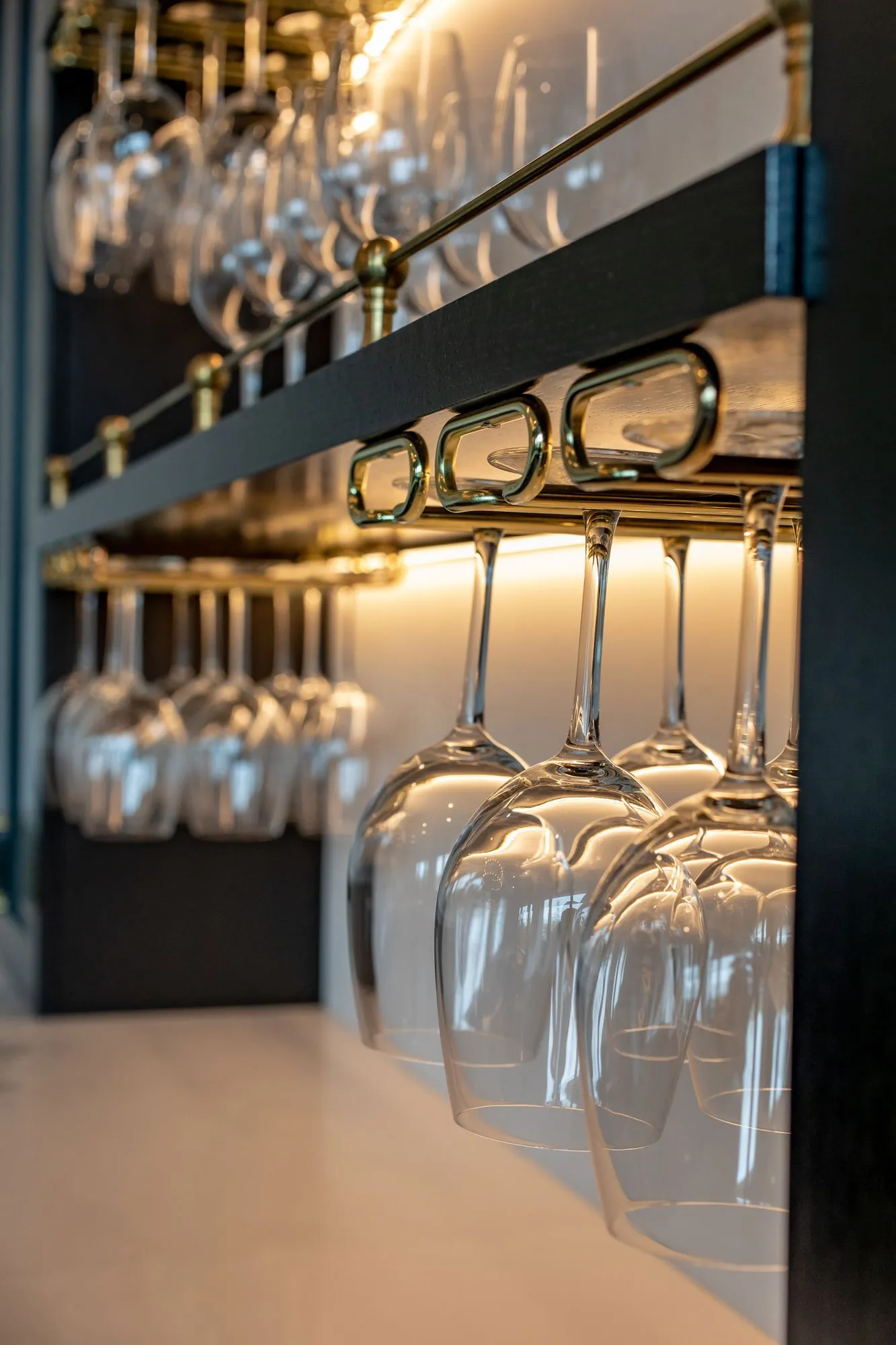 Senior living interior detail: wine glasses hanging from brass racks on black shelving
