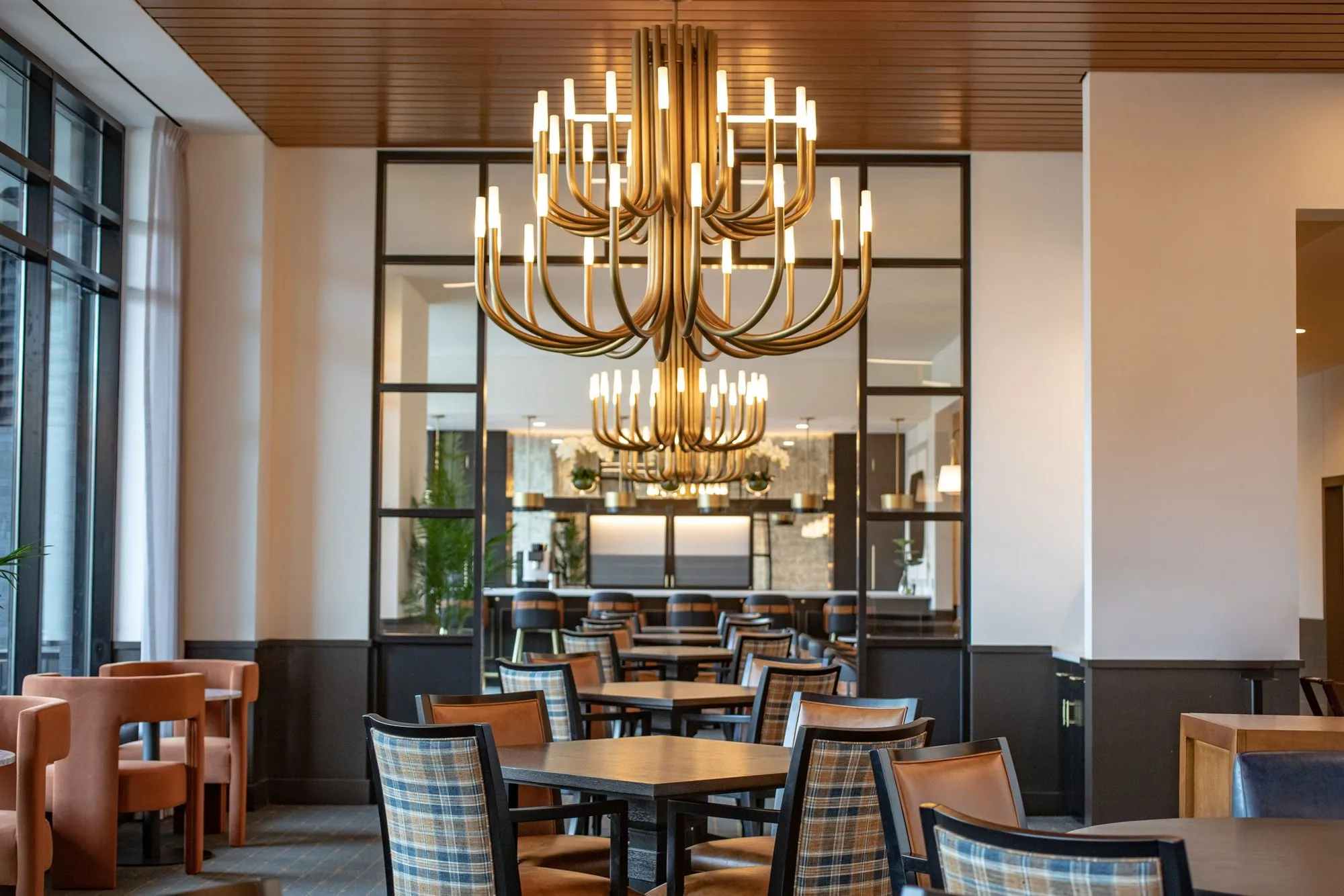 Senior living dining room with a tiered brass candle chandelier before a black framed mirror wall, plaid chairs below