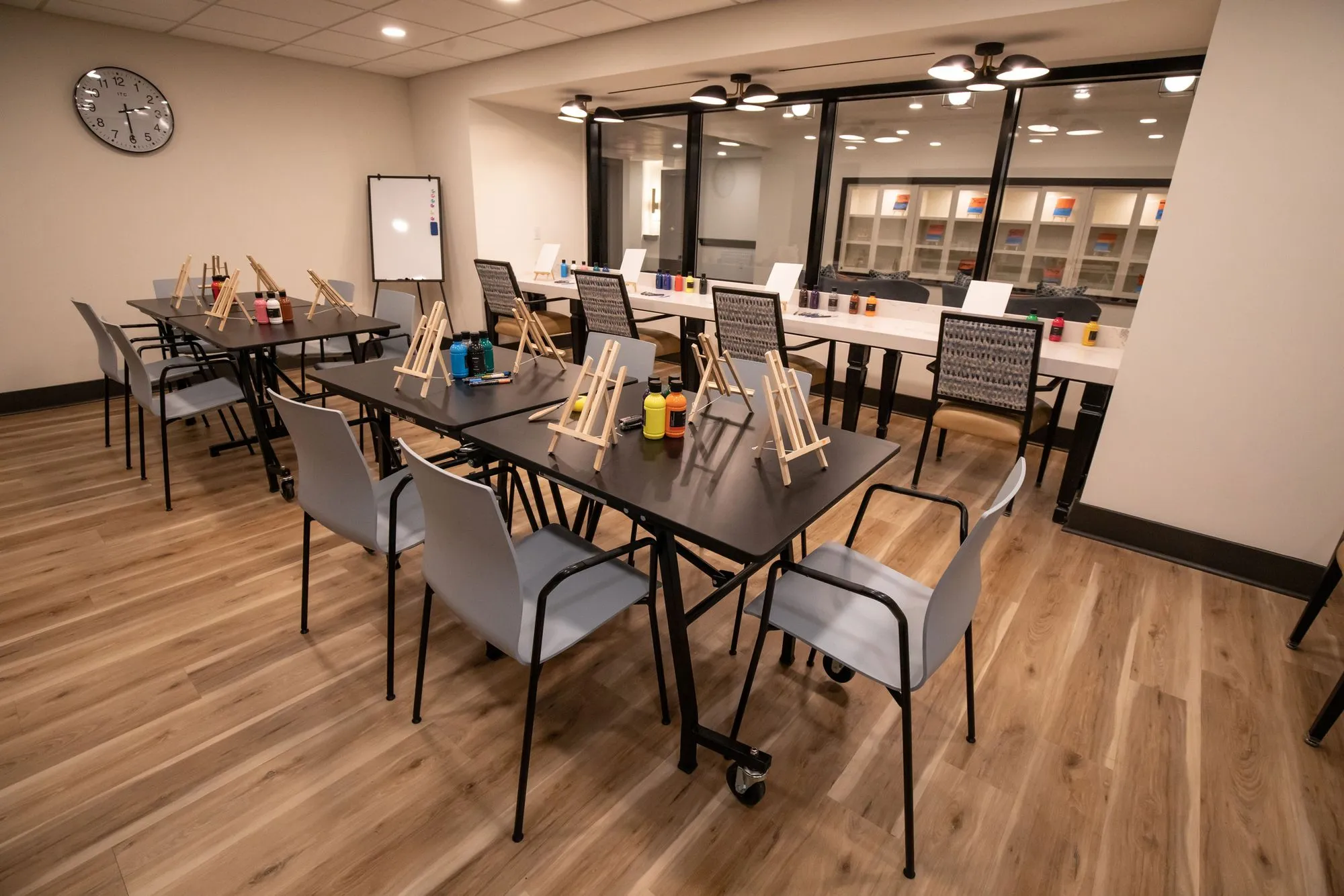 Senior living art studio with small easels and paint pots on black tables, grey chairs and a whiteboard