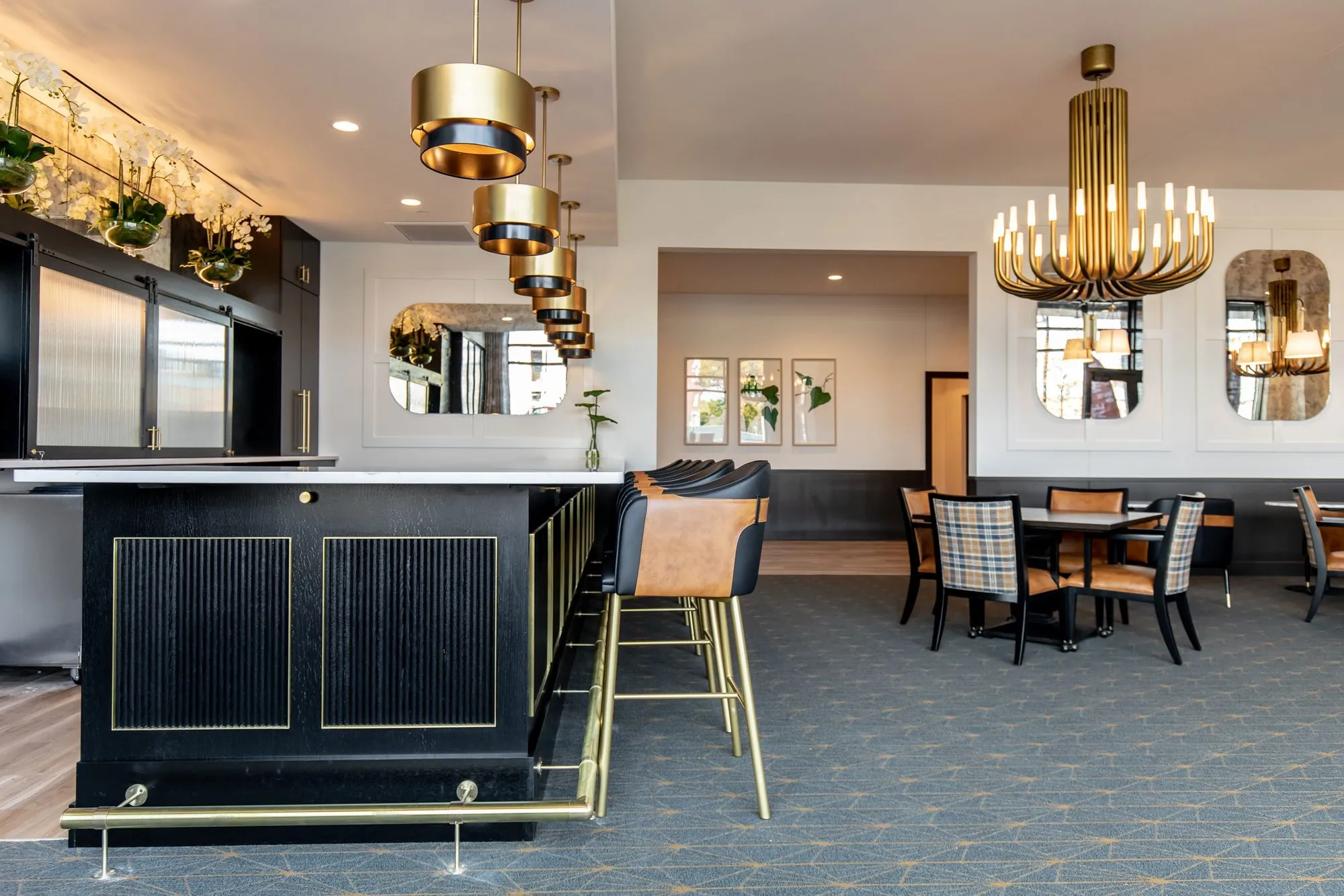 Senior living bar end, black fluted with brass trim, leather stools under brass drum pendants, dining room beyond