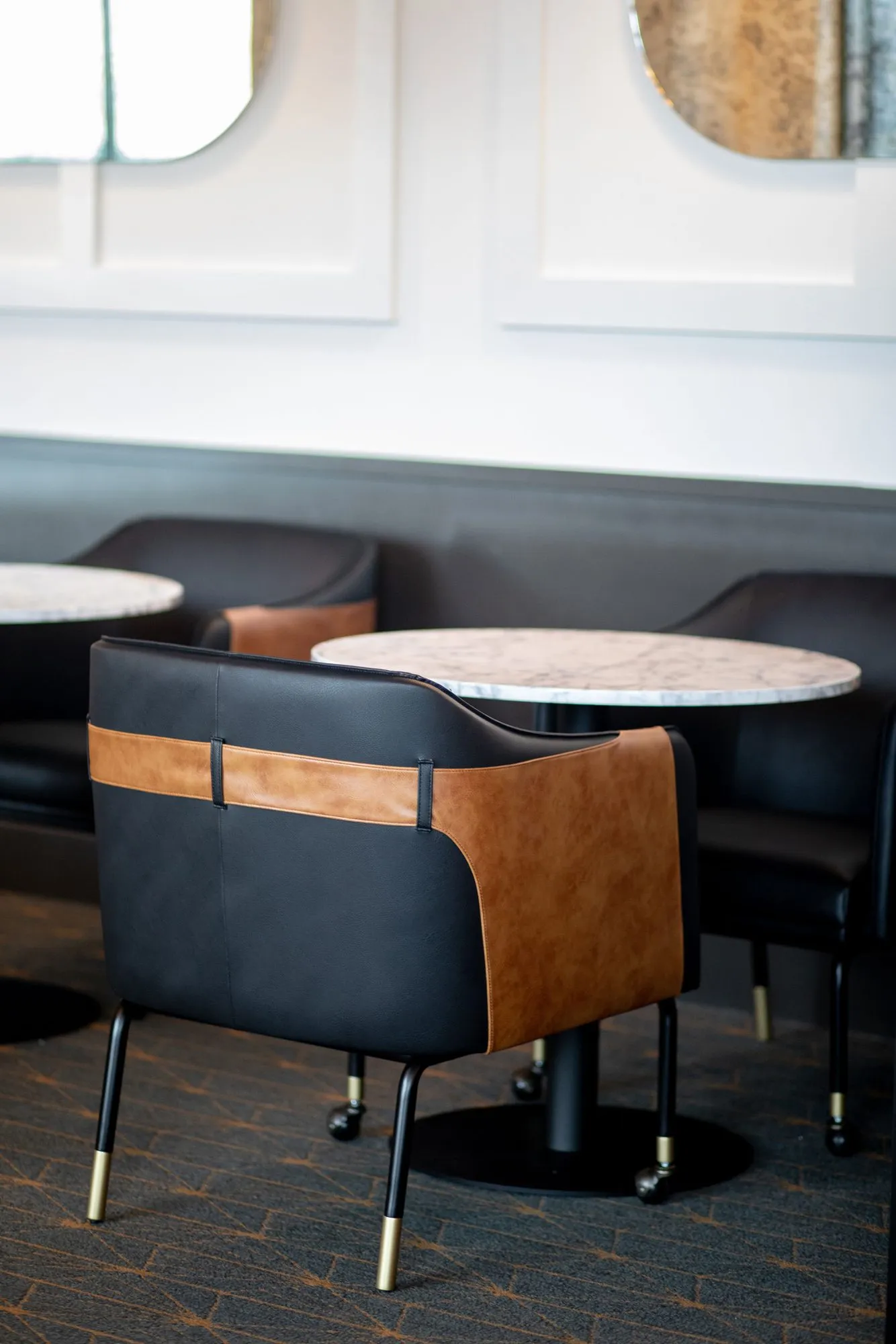 Senior living interior detail: black and cognac leather chair at a marble cafe table, banquette and arched mirrors behind
