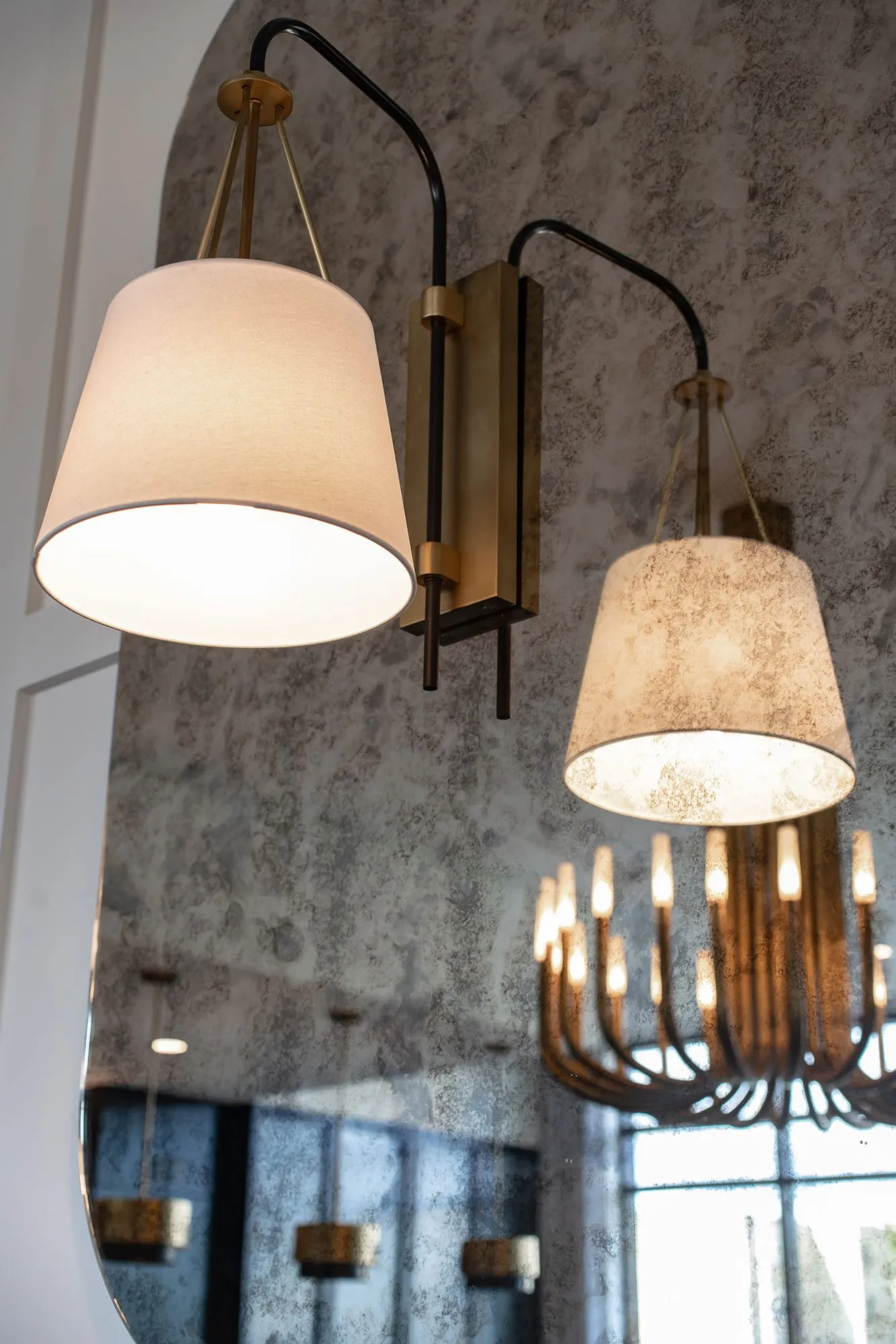 Senior living interior detail: double swing-arm sconce with linen shades on an antiqued mirror reflecting a brass chandelier