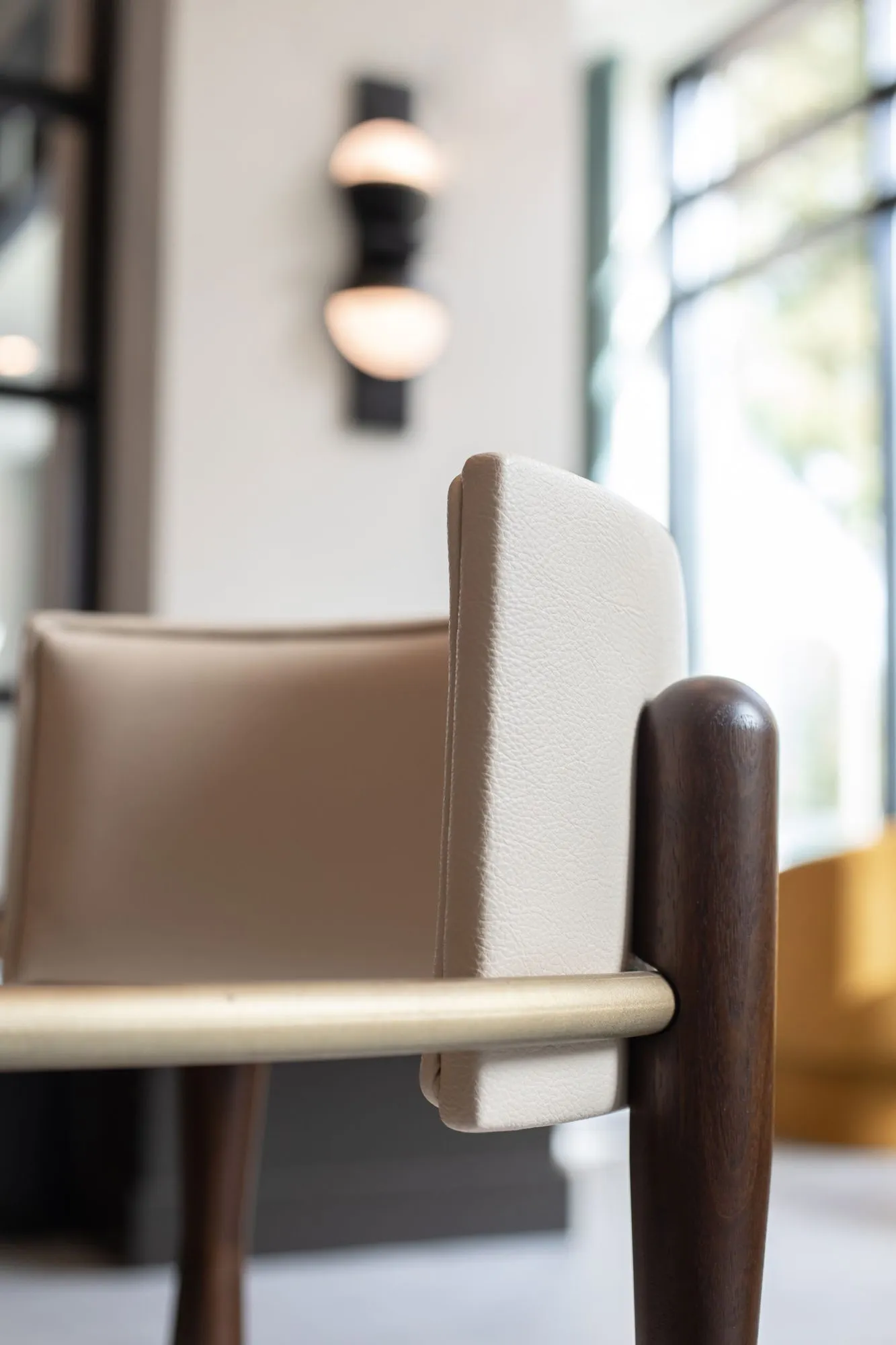 Senior living interior detail: dining chair with a cream leather back, brass arm and dark wood frame, globe sconce behind