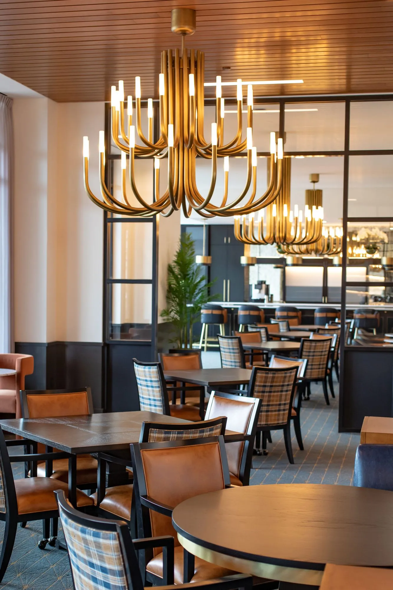 Senior living dining room with a row of brass candle chandeliers under a wood slat ceiling, plaid and leather chairs