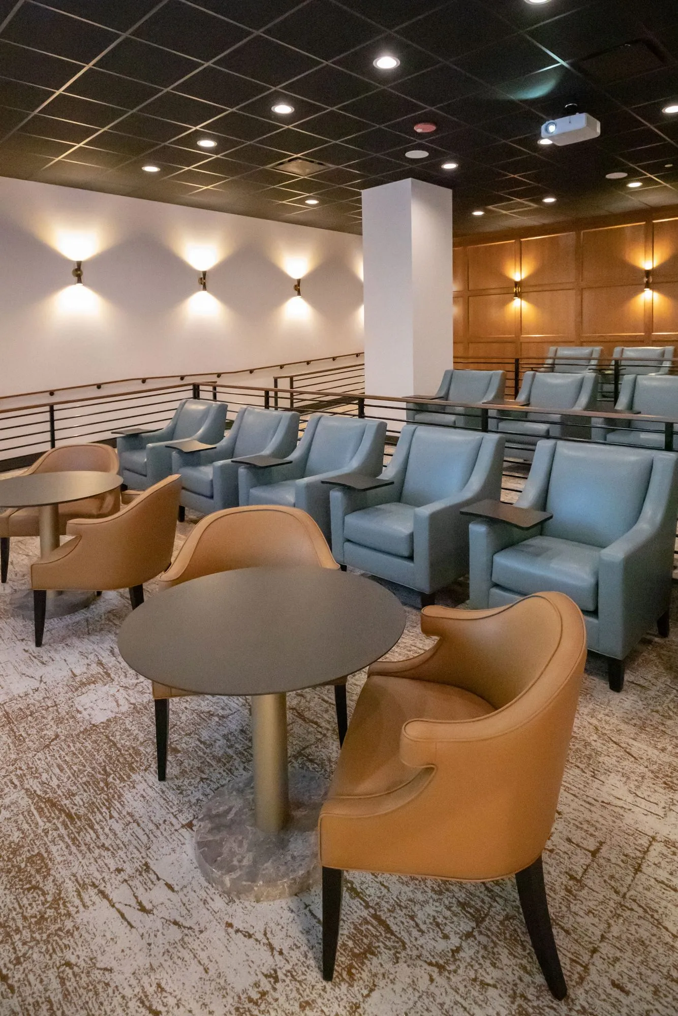 Senior living theatre: tan leather chairs at cafe tables behind tiered rows of blue-grey seating and uplit sconces