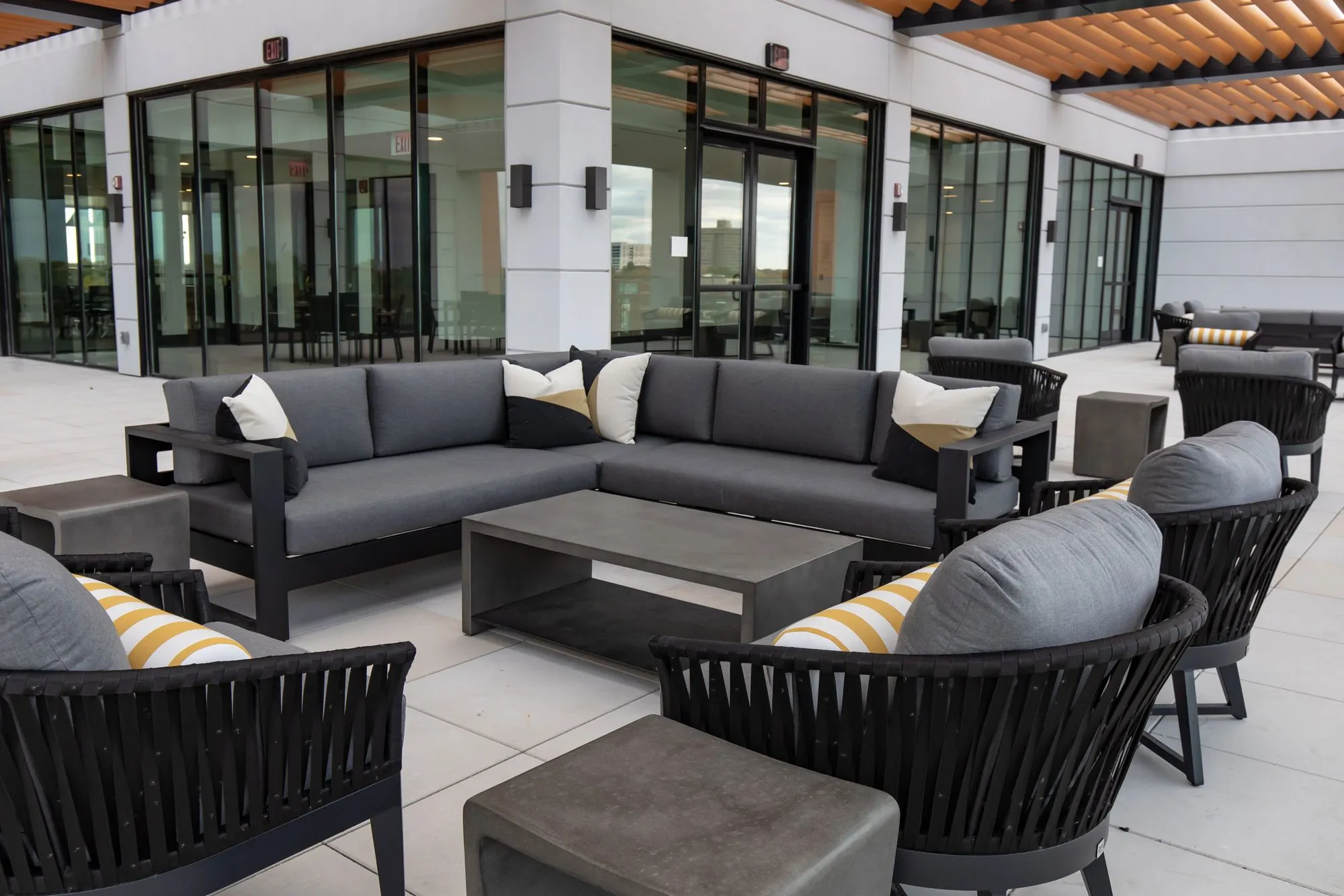 Senior living outdoor seating: grey sectional and black rope chairs around a concrete table before glass doors