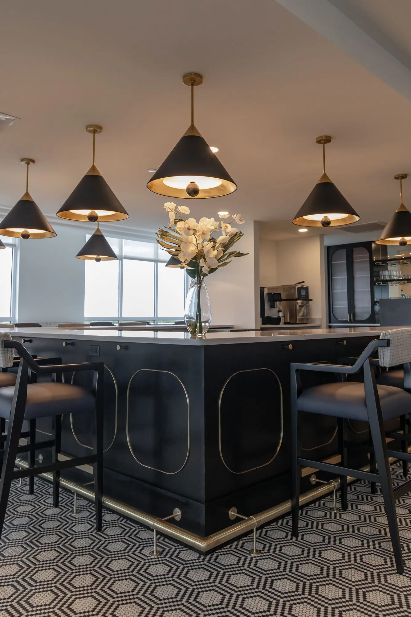 Senior living bar in black with brass inlaid panels under cone pendants and orchids, black bar stools on hexagon tile