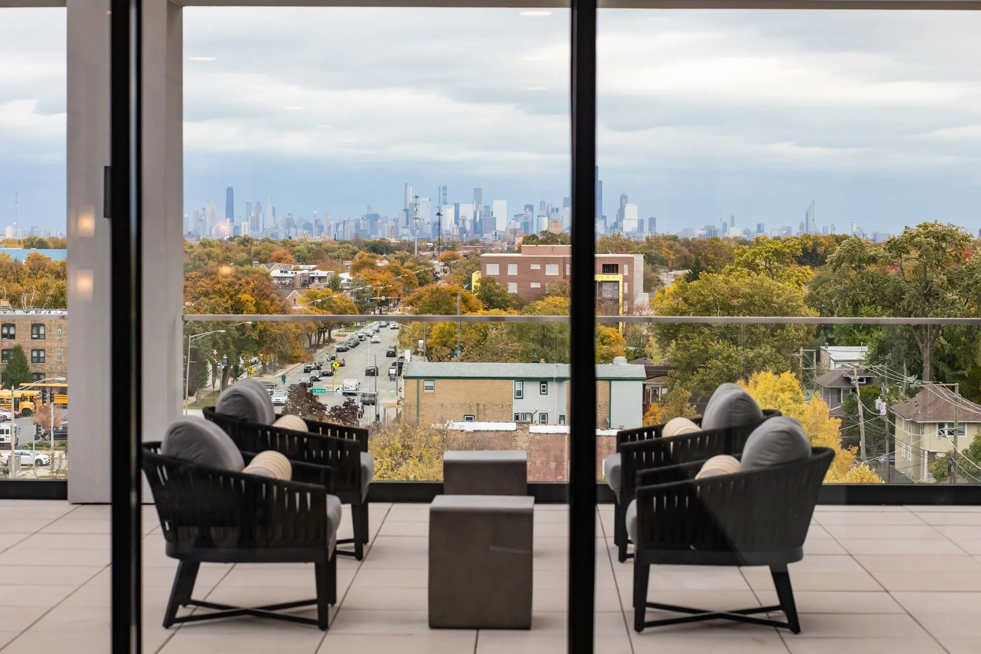 Senior living outdoor seating: rope lounge chairs and a concrete table through open sliding doors, downtown skyline beyond