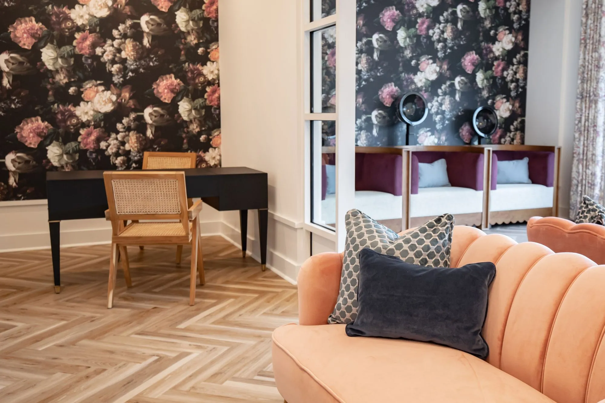 Senior living salon with a peach channel back sofa, a cane chair at a navy desk and dark floral wallpaper