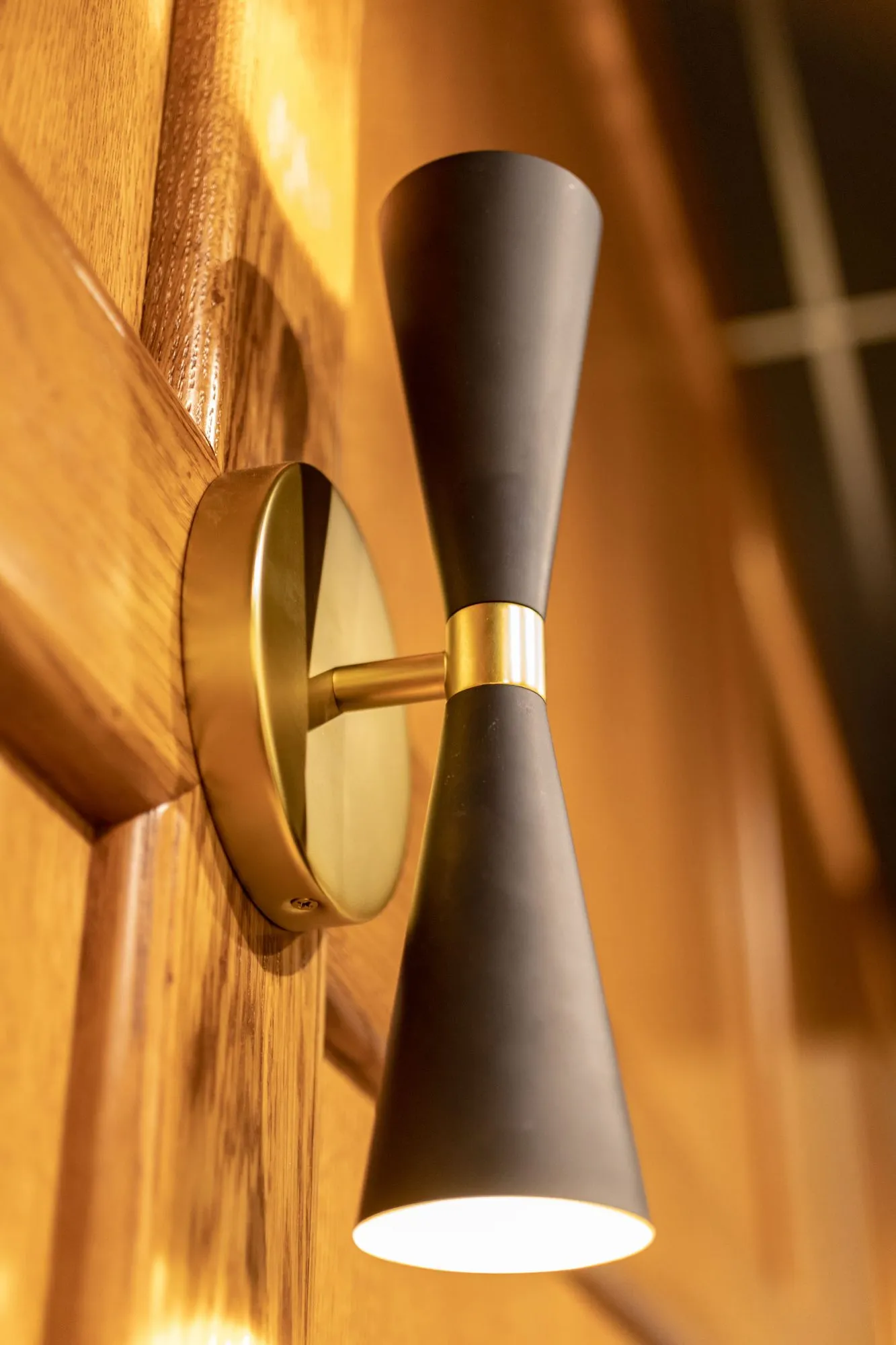 Senior living interior detail: warmly lit black and brass hourglass sconce on oak panelling