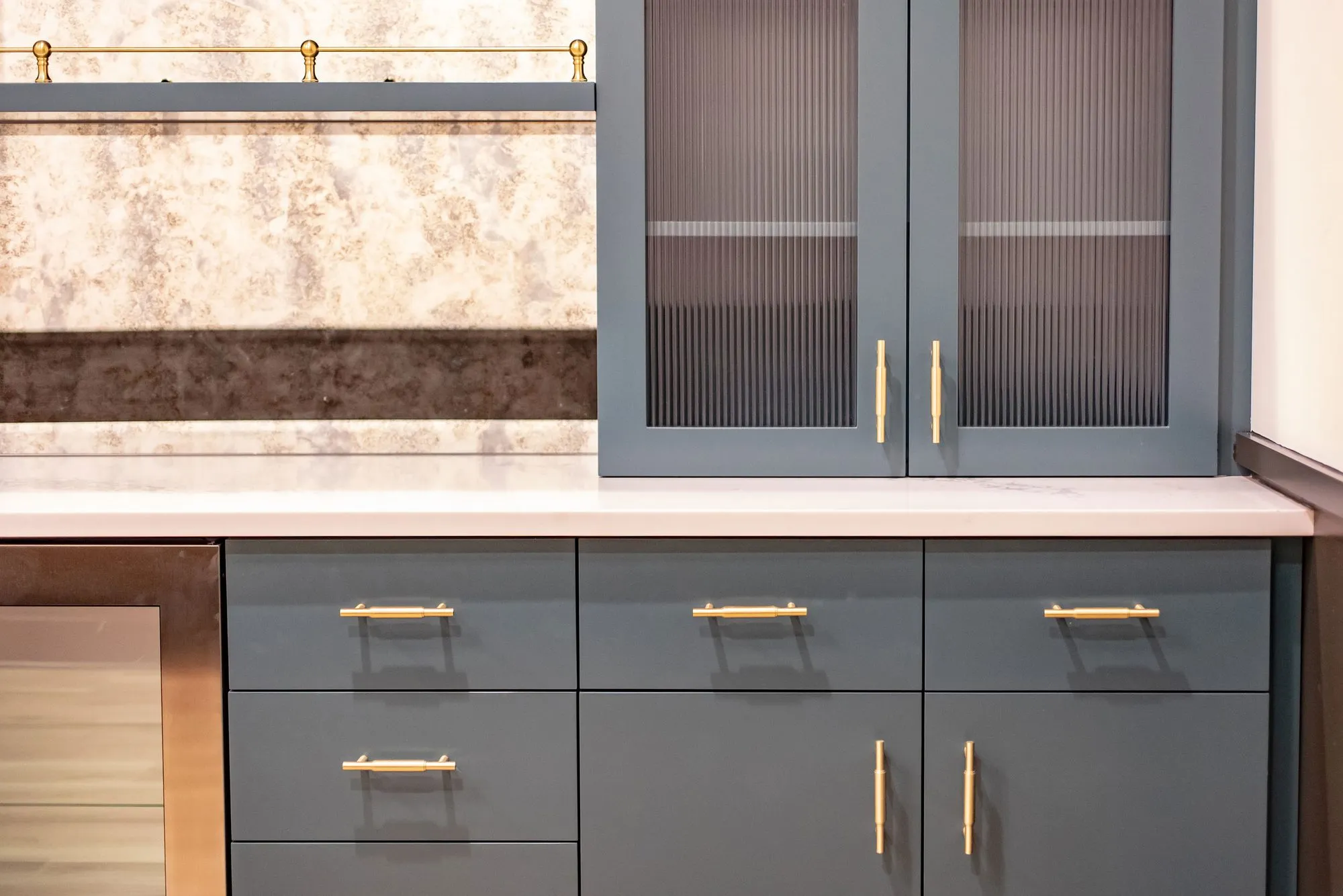 Senior living interior detail: slate blue cabinetry with brass pulls and reeded glass doors by an antiqued mirror backsplash