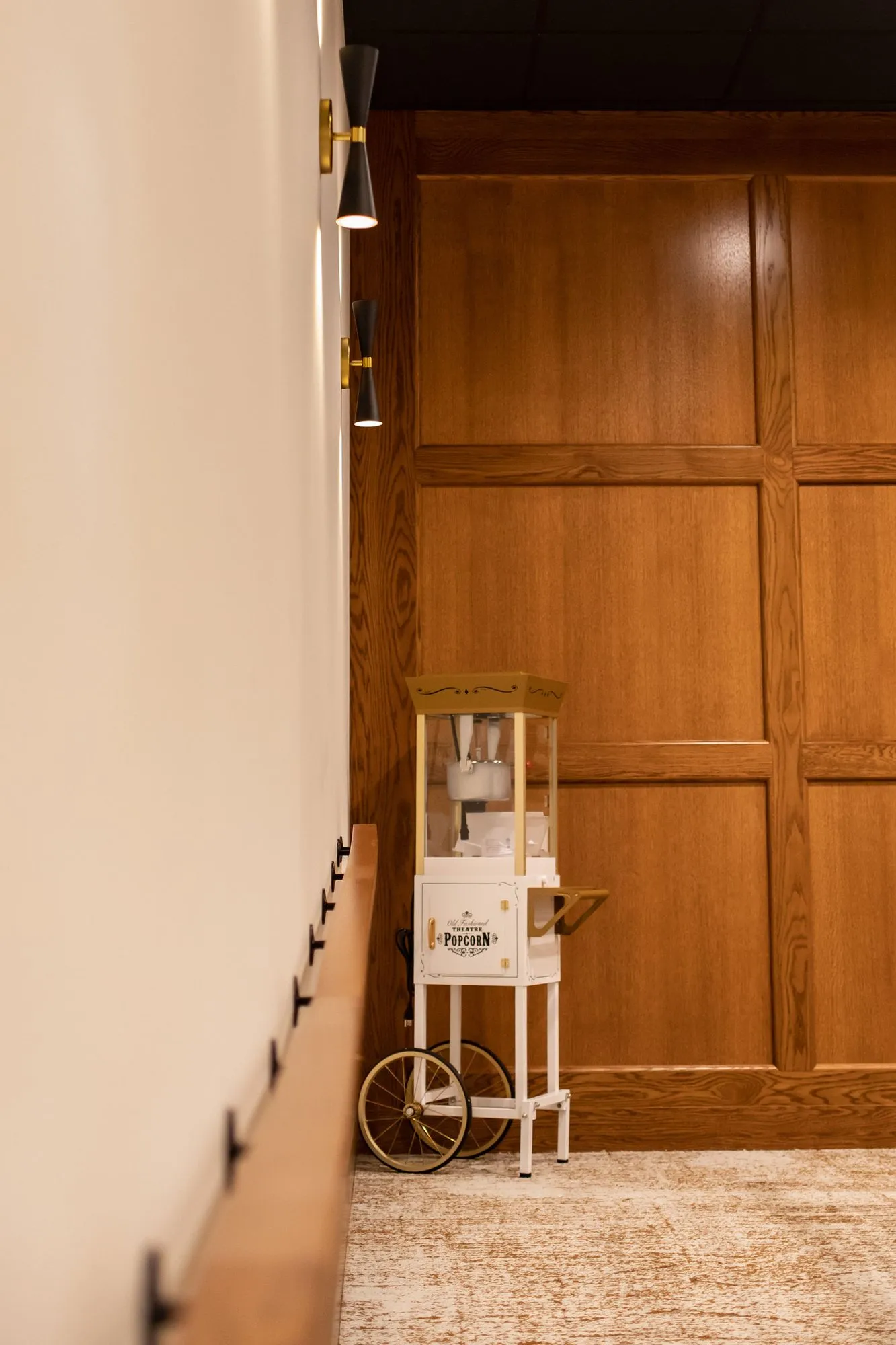 Senior living interior detail: popcorn cart against oak panelling at the end of a white wall with black and brass sconces