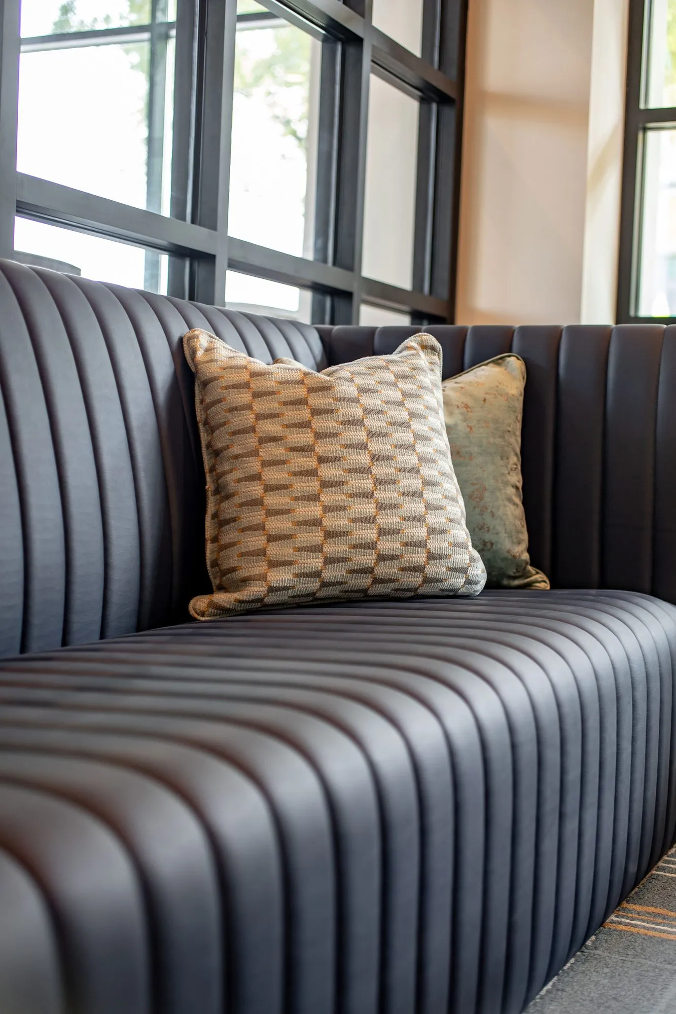 Senior living interior detail: charcoal channel tufted banquette with patterned pillows by black framed windows