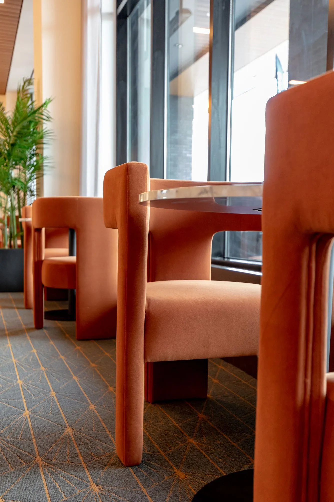 Senior living dining room with rust velvet sculptural chairs at marble tables along the windows