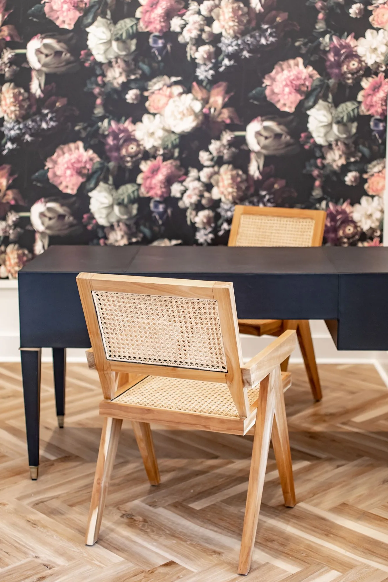 Senior living interior detail: cane back chair at a navy desk against dark floral wallpaper on a herringbone floor