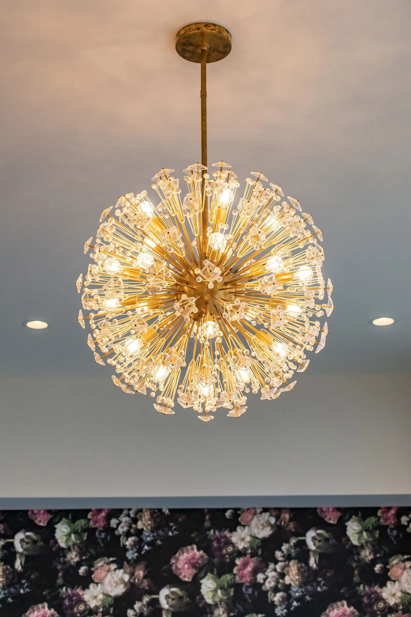 Senior living interior detail: gold starburst chandelier with crystal tips above a band of dark floral wallpaper