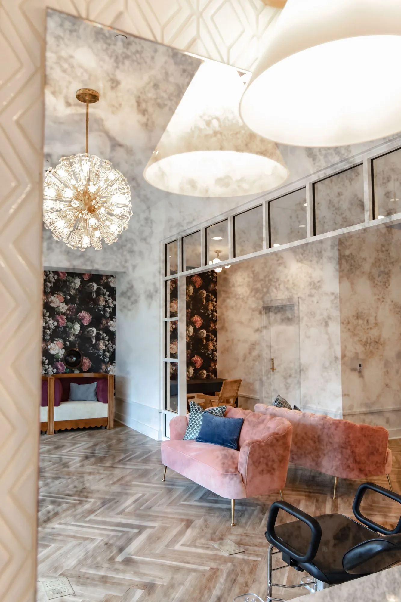 Senior living salon reflected in a mirror, with a starburst chandelier, blush velvet chairs and floral wallpaper panels