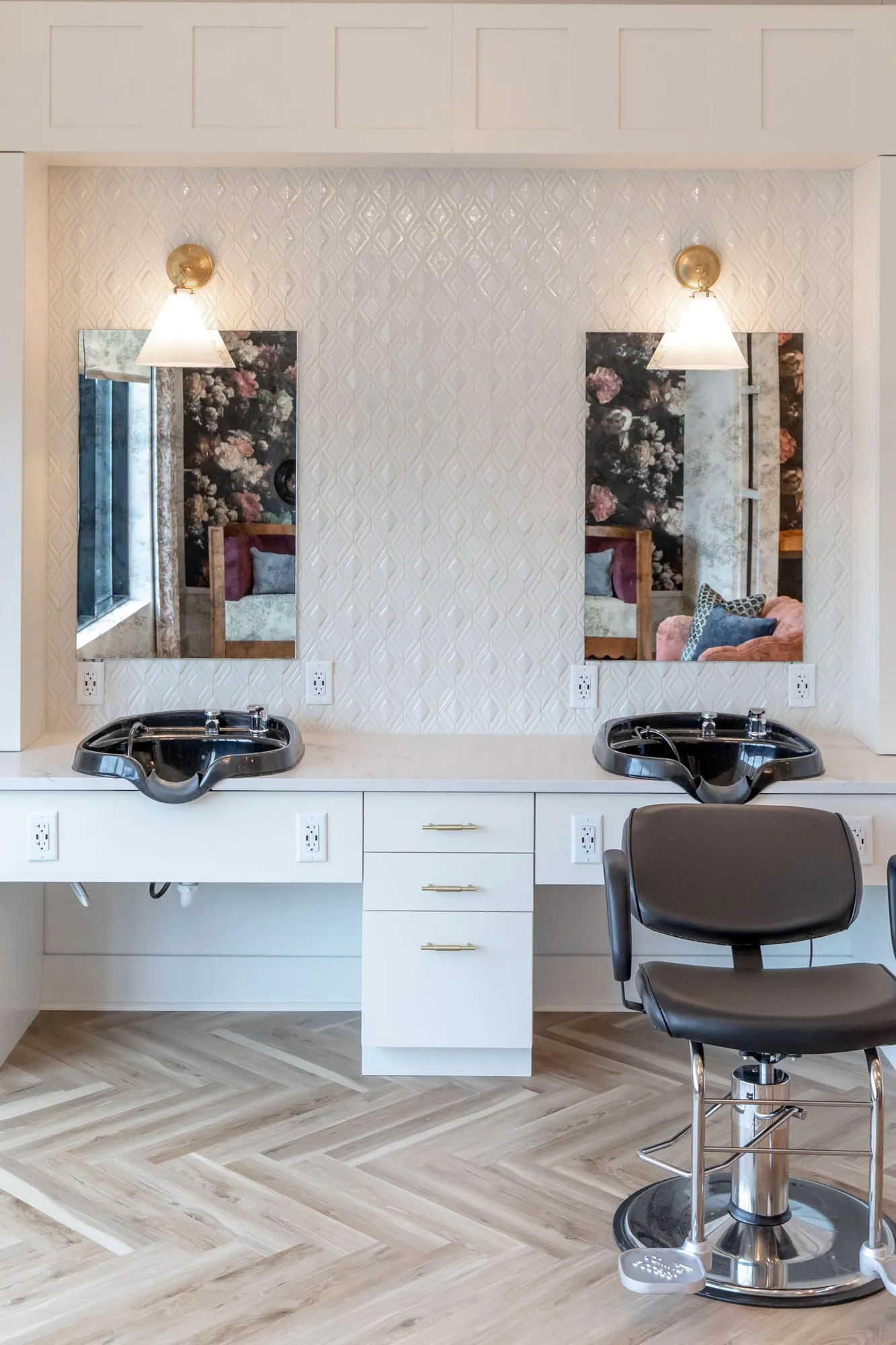 Senior living salon with two black shampoo basins on a white vanity below brass sconces and mirrors, a styling chair