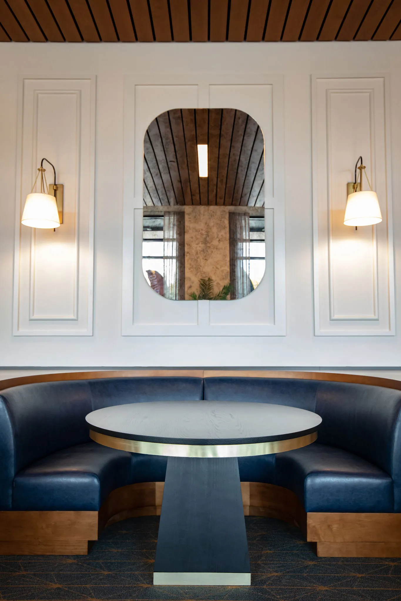 Senior living dining booth with a curved navy leather banquette below an arched mirror set between sconces