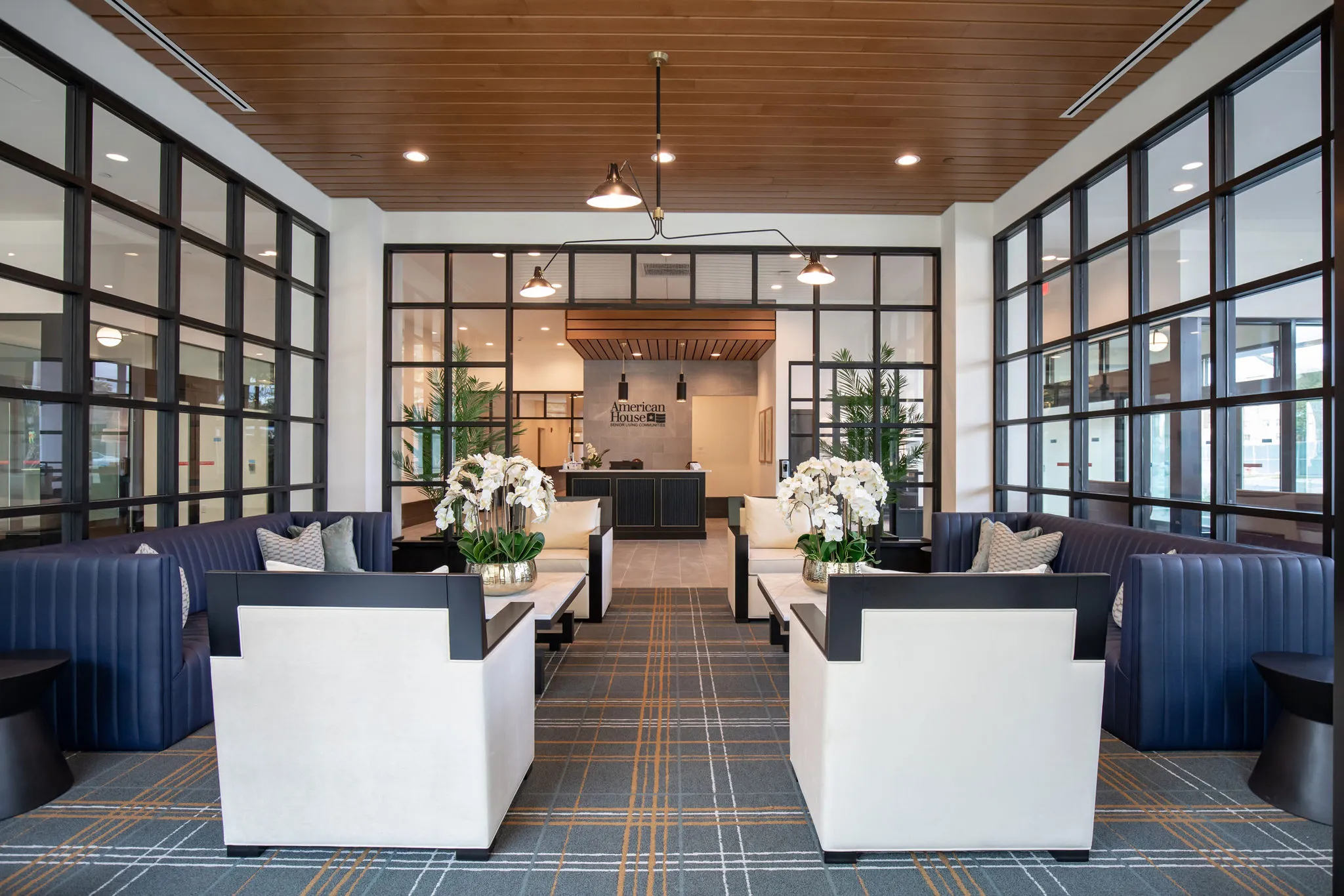 Senior living club room with navy banquettes and white armchairs framed by steel-framed glass partitions