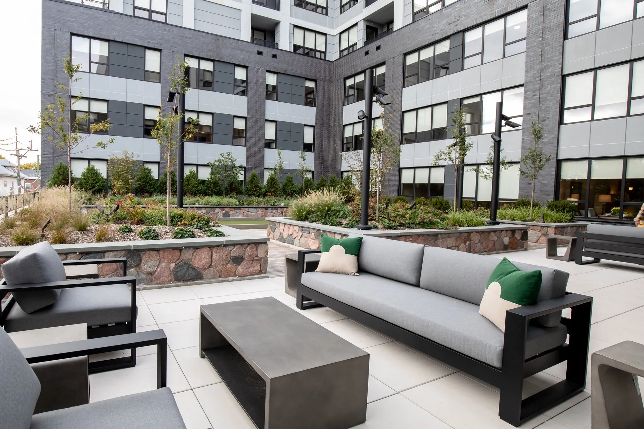 Senior living courtyard with grey sofas and concrete tables against planted stone beds below the residences