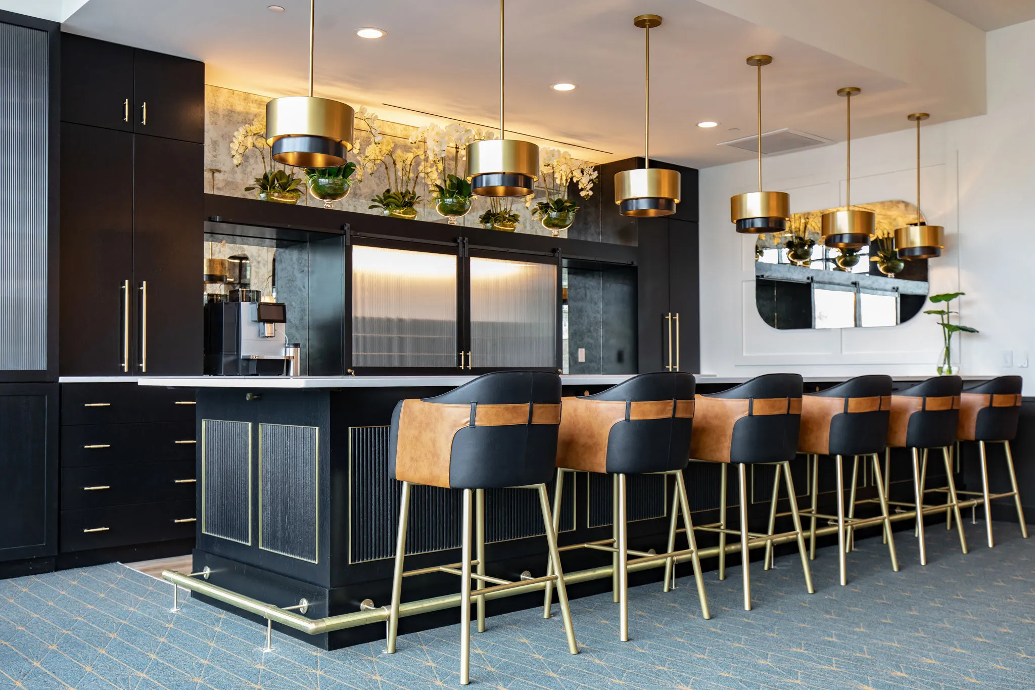 Senior living custom bar with ebony millwork and brass shelving above camel leather stools on slim brass legs