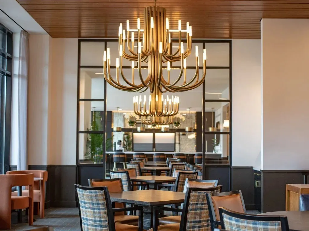 Senior living dining room at American House Oak Park with two brass candelabra chandeliers and plaid chairs at wood tables