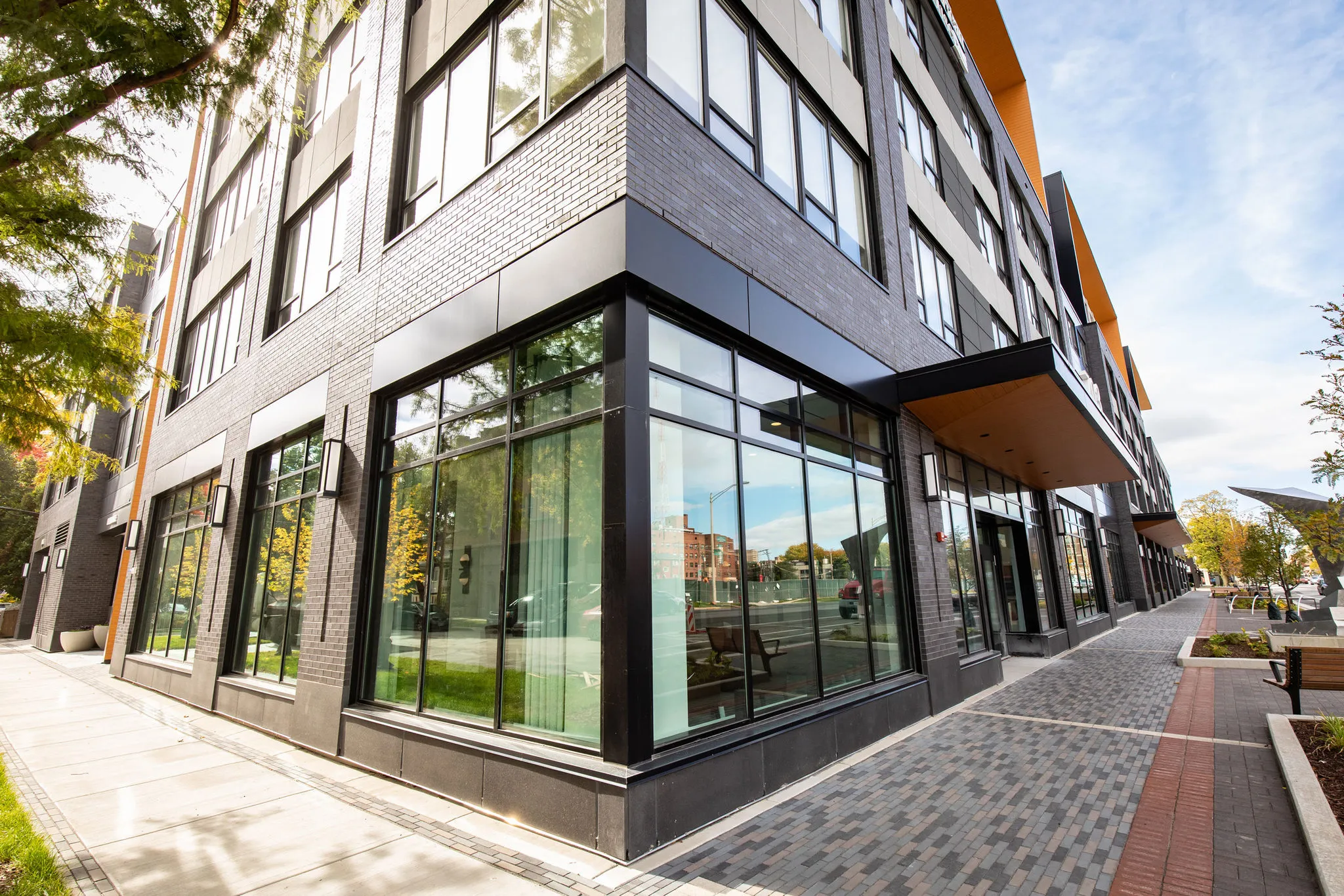 Senior living community exterior: black steel storefront glazing wrapping the brick corner of the building on the street