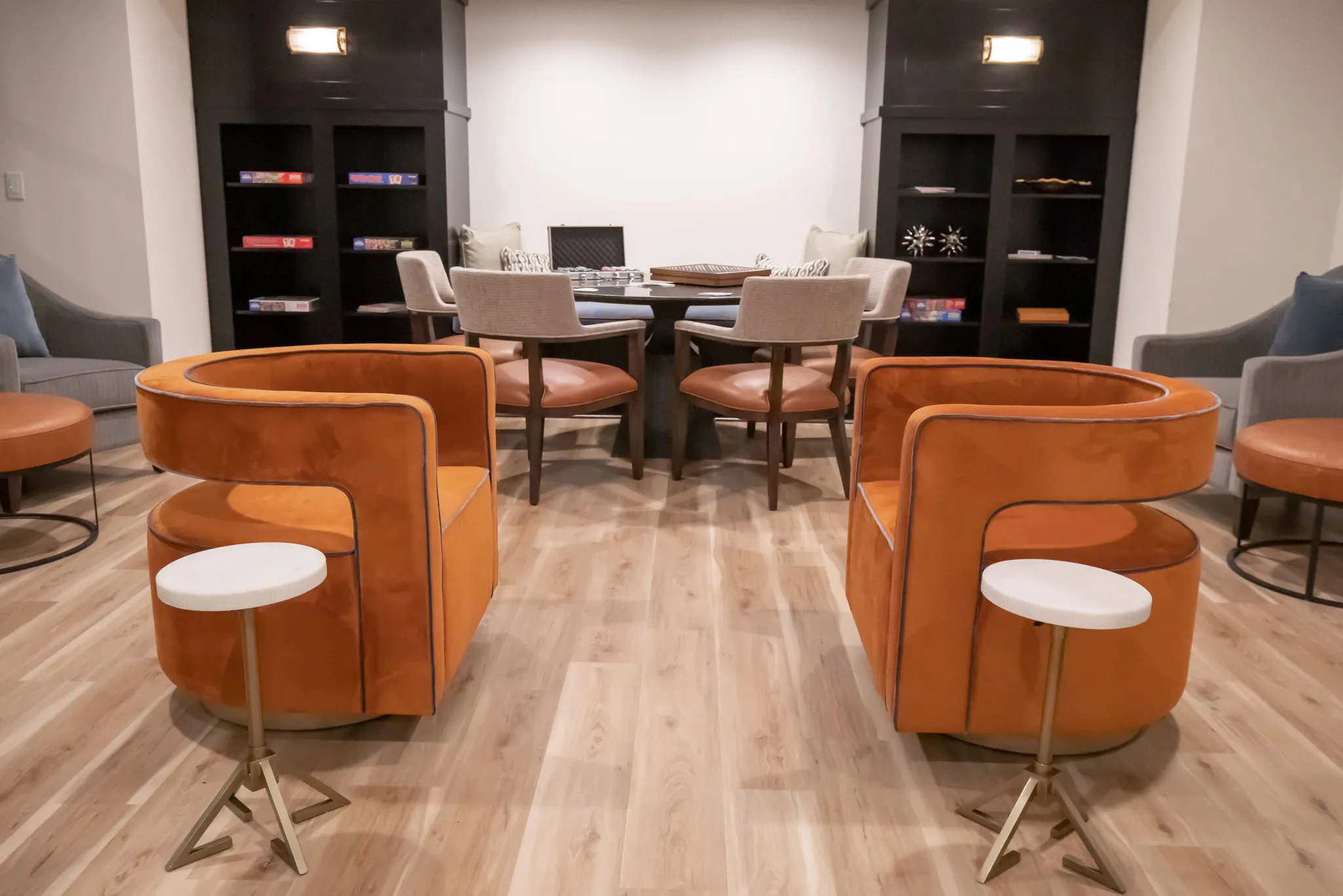 Senior living game room with burnt orange swivel chairs and a card table between black bookcases