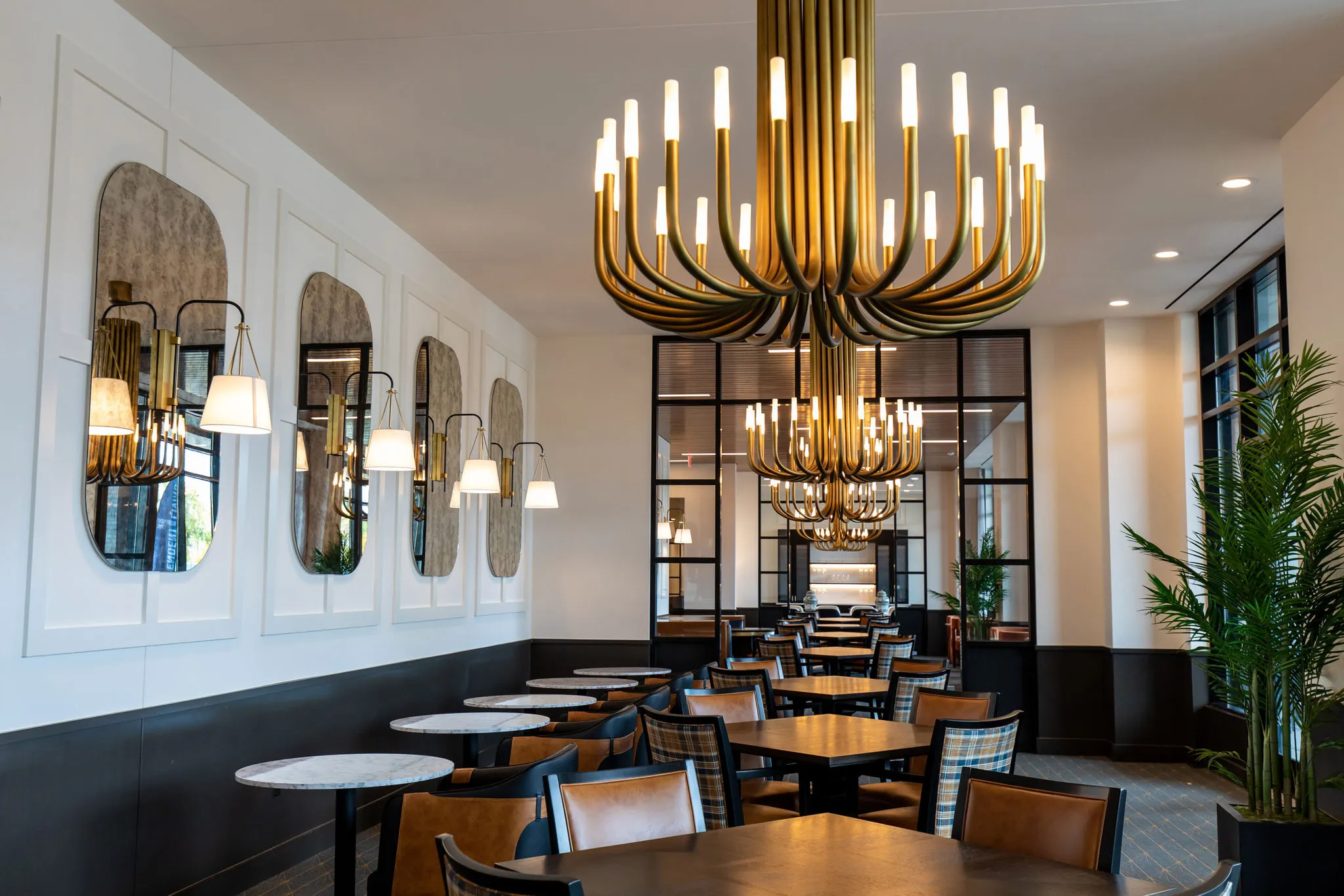 Senior living dining room with a tiered brass candle chandelier, arched mirrors and sconces on white panelled walls