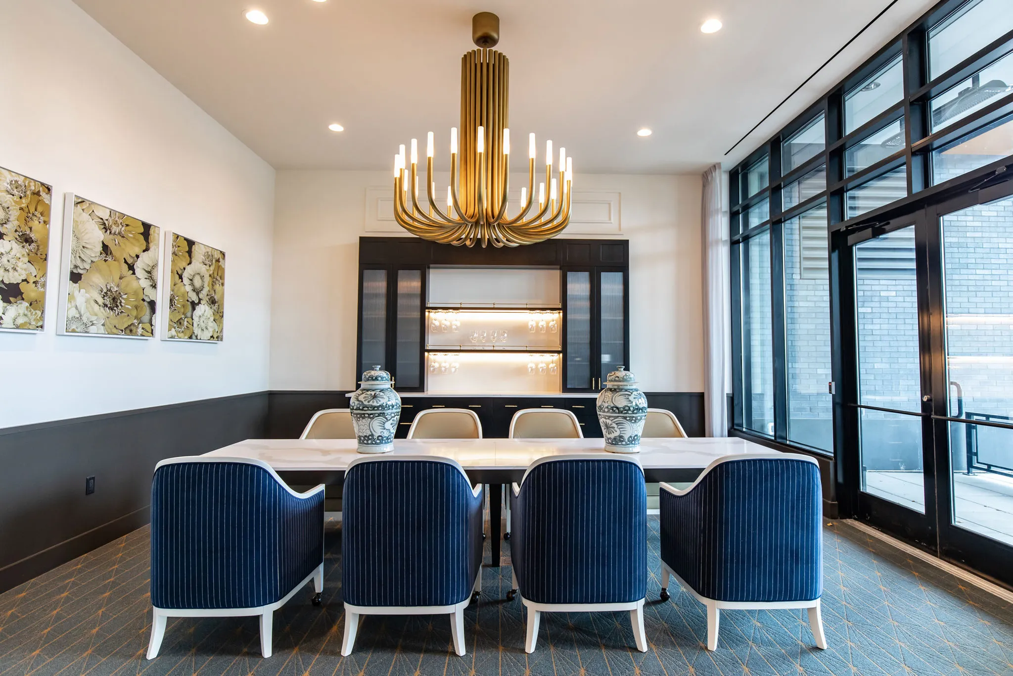 Senior living private dining room with navy channel-back chairs along a marble table under a brass chandelier