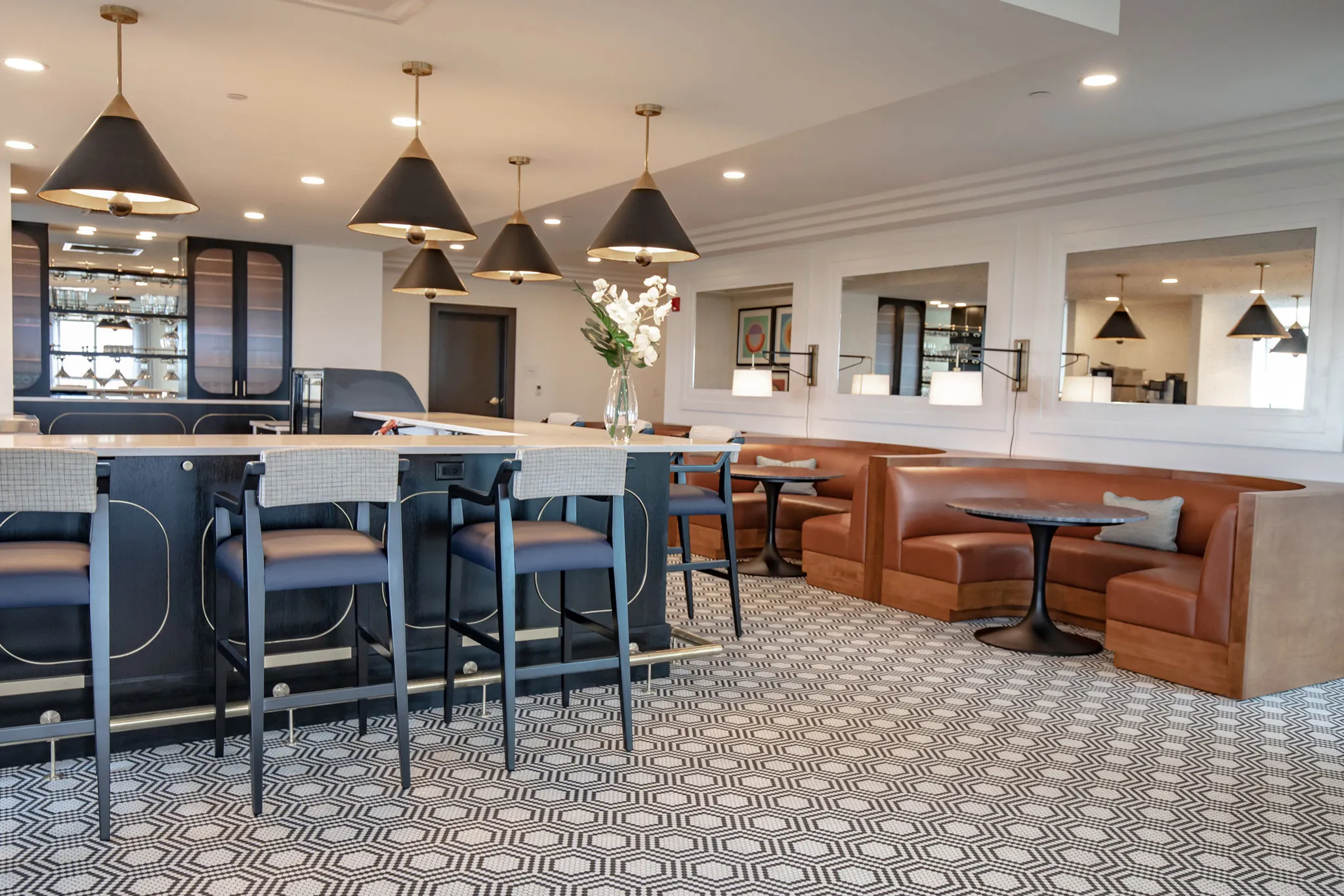 Senior living bistro with black cone pendants over the bar and cognac leather banquettes on geometric tile