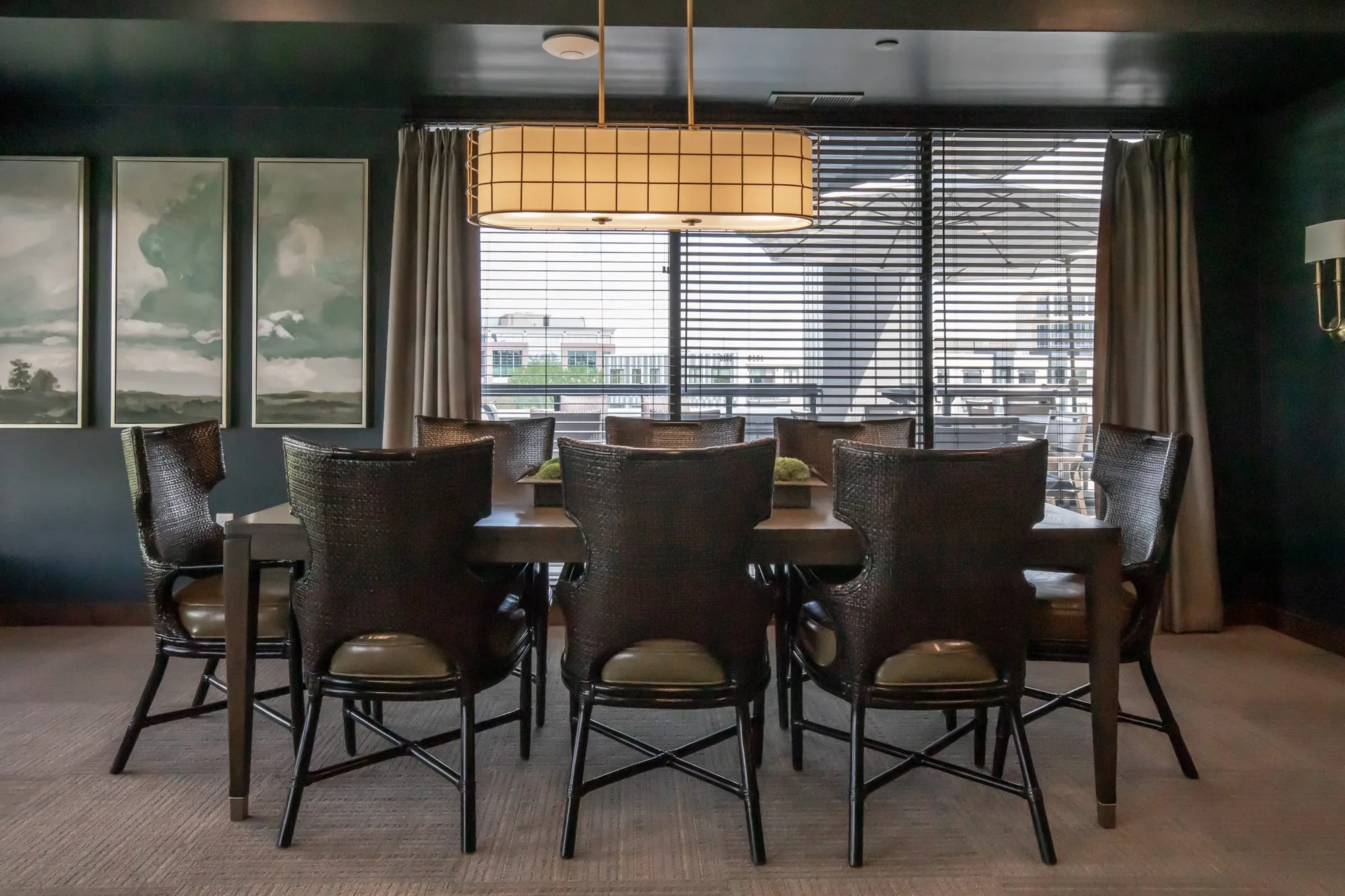 Active adult community dining room with woven wingback chairs at a long table under a lantern, prints on dark green walls