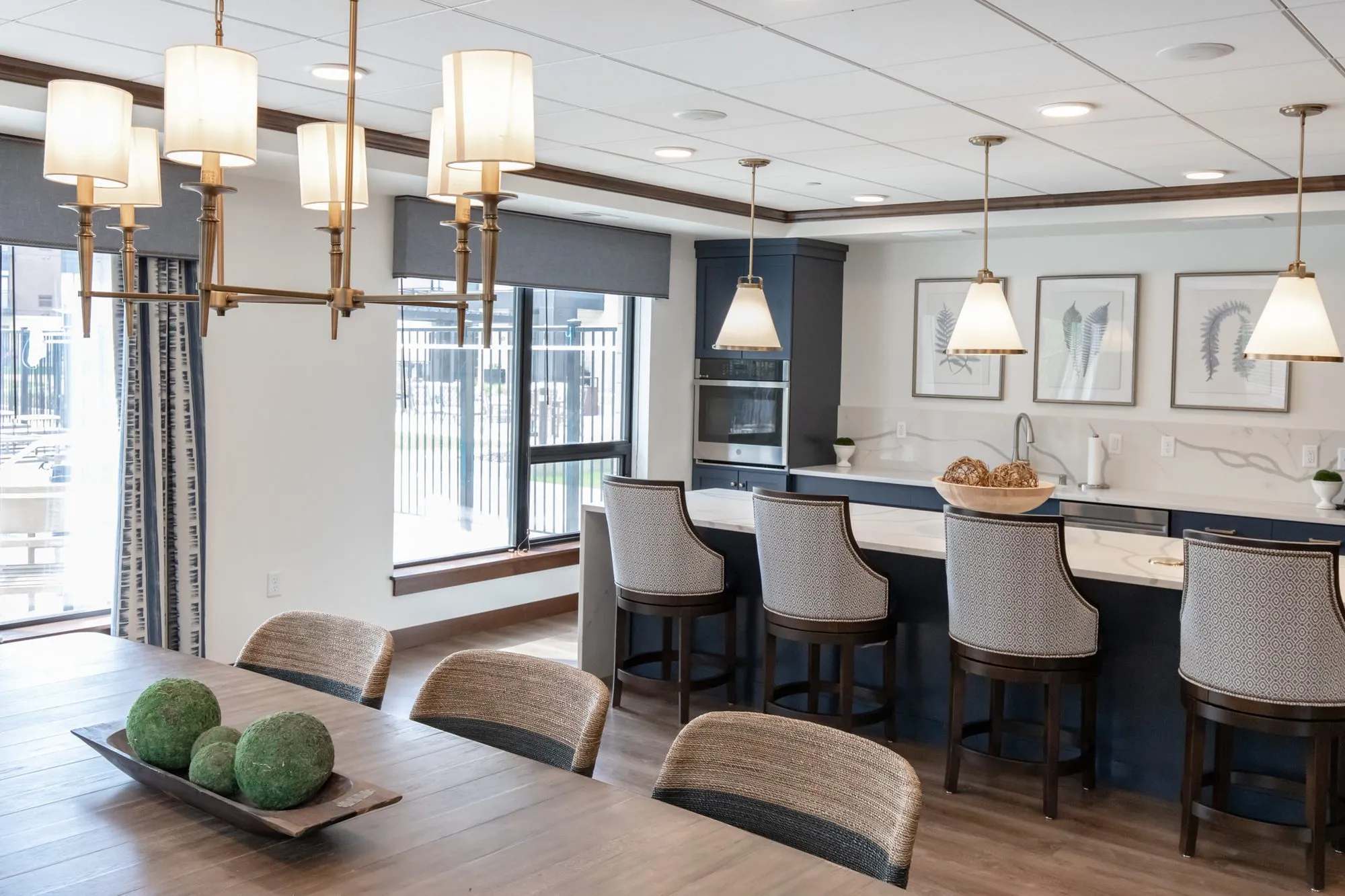 Active adult community dining table under a brass shaded chandelier, a navy kitchen island with stools and pendants beyond