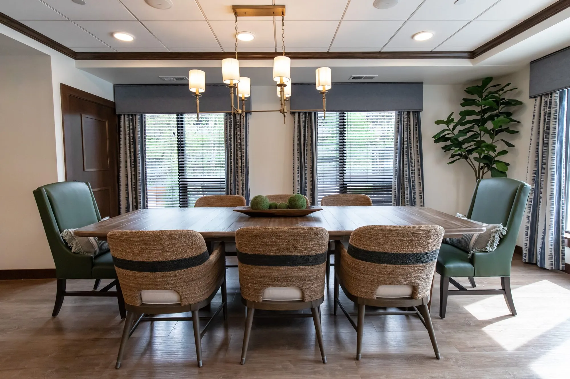 Active adult community private dining room with woven chairs and green leather host chairs at a wood table under a chandelier
