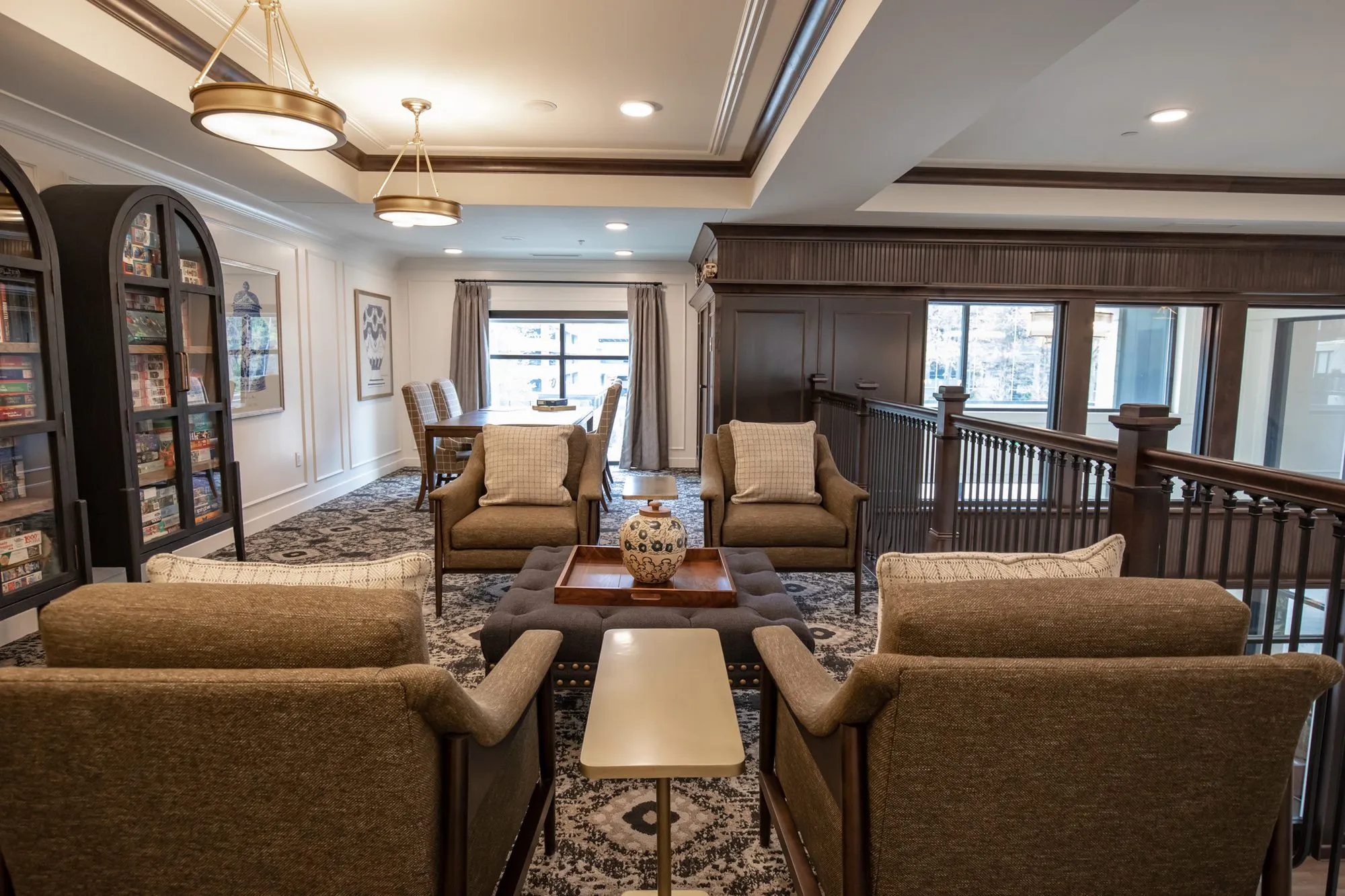 Active adult community upper landing lounge with tan armchairs around a tufted ottoman beside arched bookcases