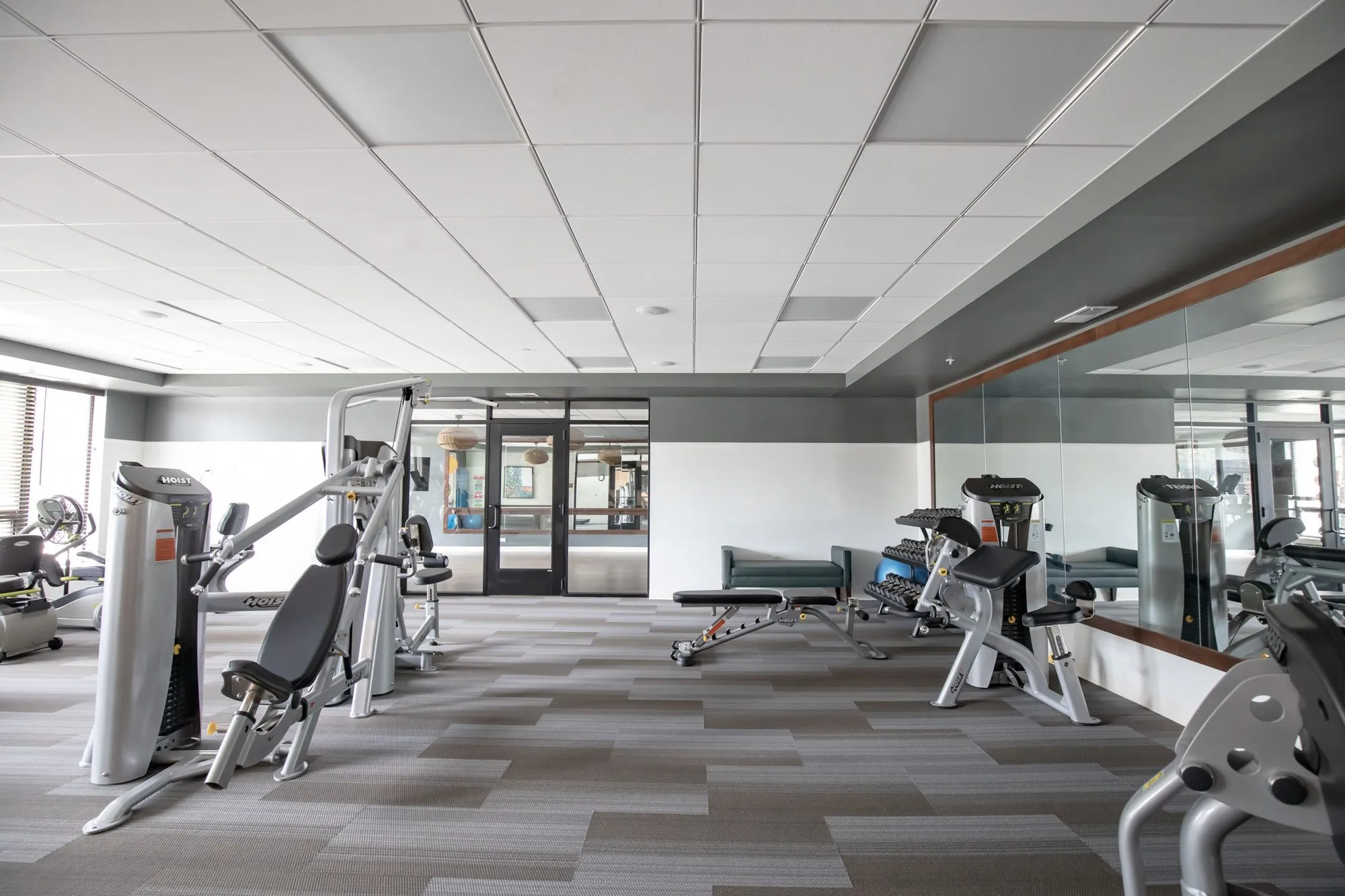 Active adult community fitness centre with strength machines on grey striped carpet beside a mirrored wall