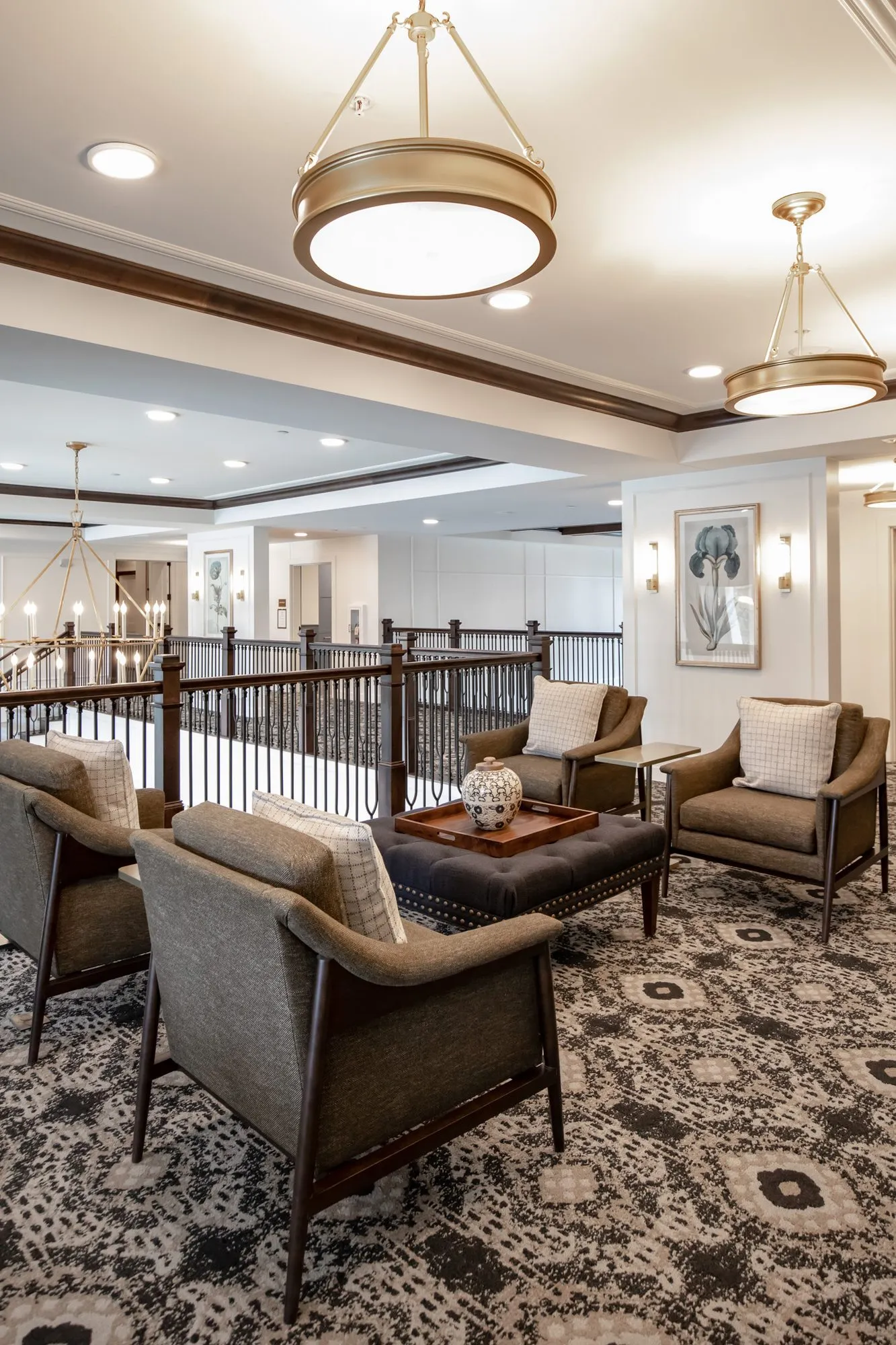 Active adult community mezzanine lounge with grey armchairs around a tufted ottoman under brass pendants